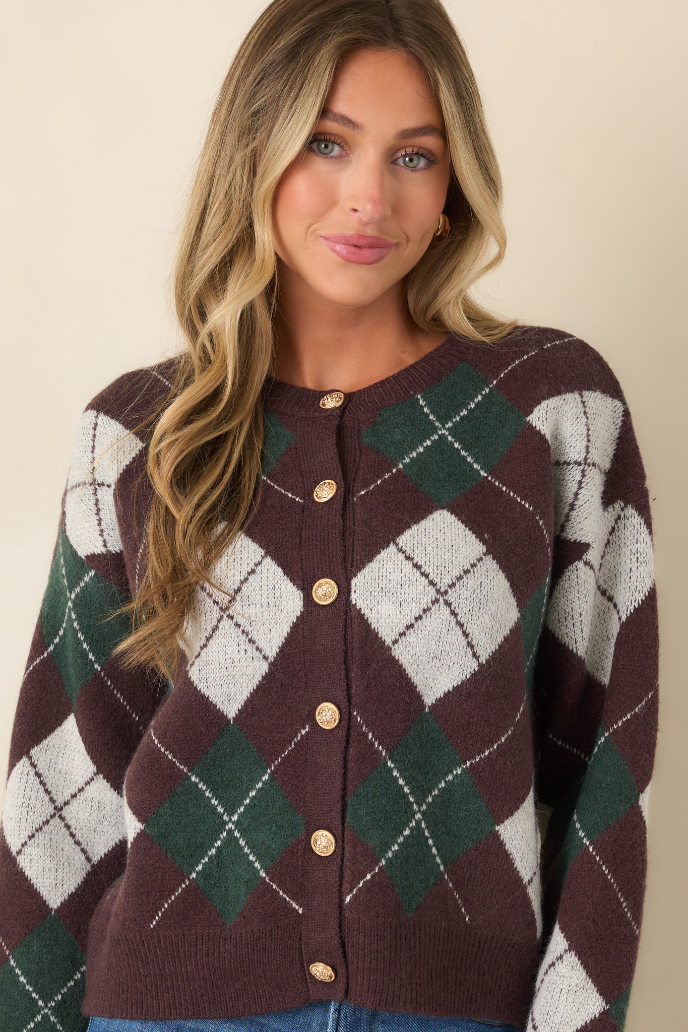 Detailed view of the knit cardigan featuring deep brown, hunter green, and ivory argyle motifs with ribbed trim.