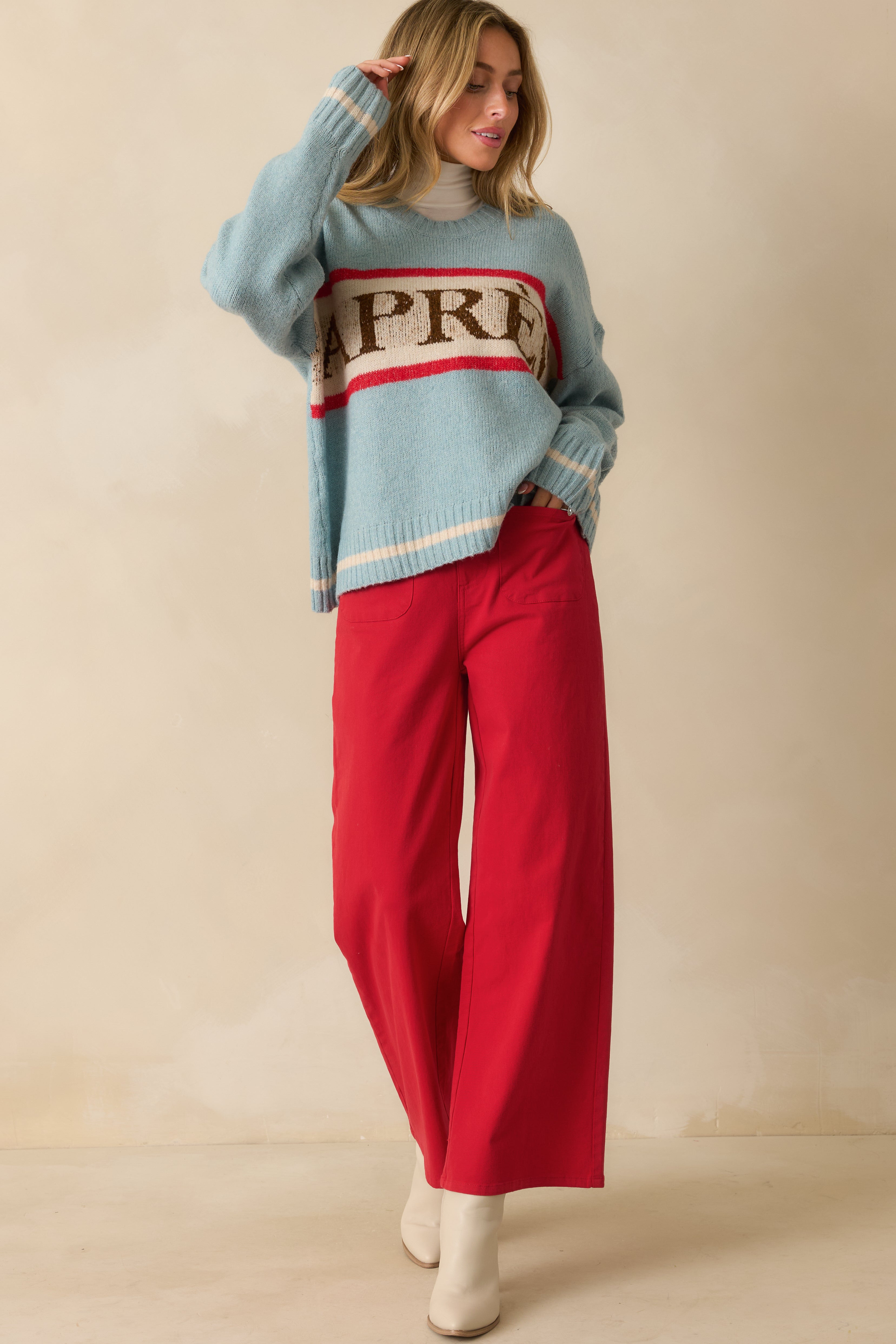 Blue knit sweater with comfortable silhouette, playful “APRÈS” lettering, and red and ivory stripe details.