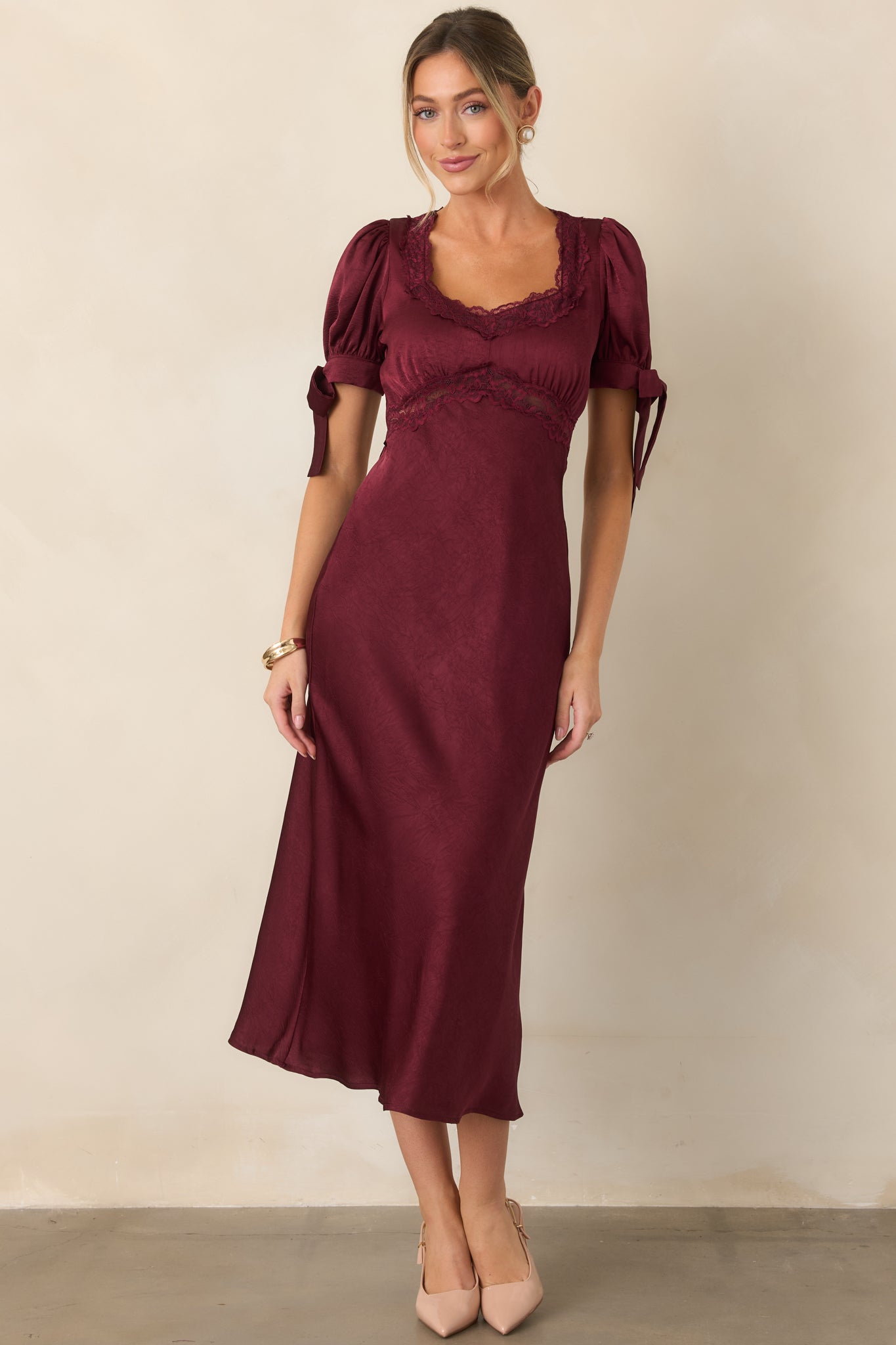 Elegant midi dress with a lace-trimmed neckline, softly gathered empire waist, voluminous short sleeves, and flowing jewel-tone satin skirt.