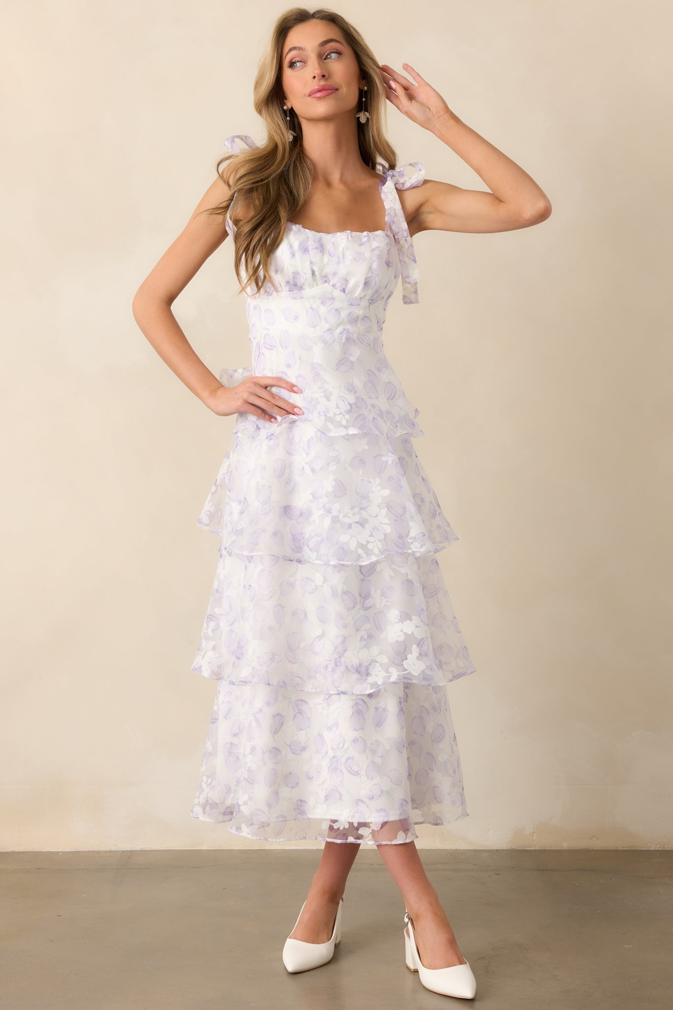 A lavender midi dress with a sheer floral tulle overlay, a sweetheart neckline, and a fitted bodice. The adjustable bow straps add a delicate, customizable touch.