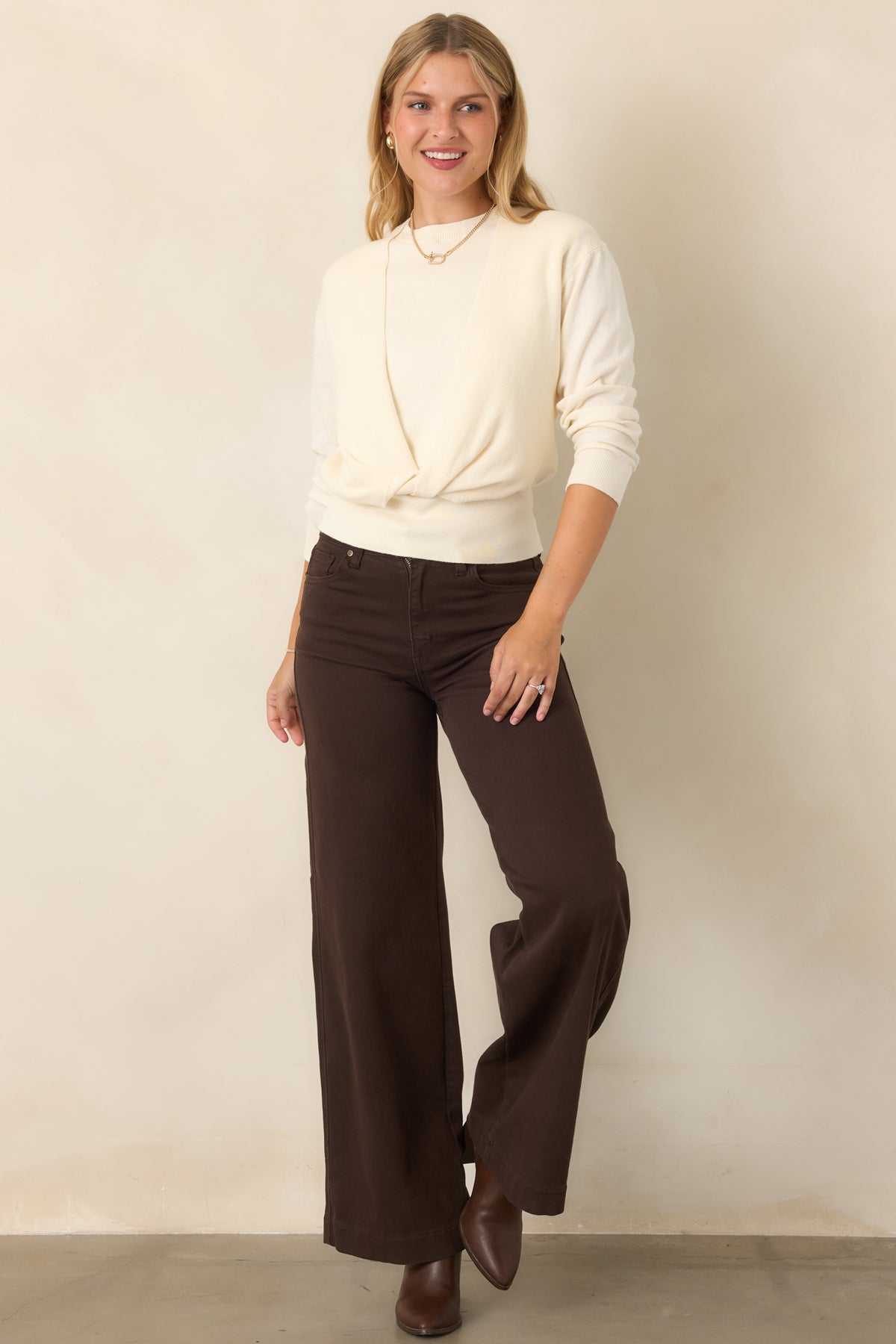 Layered knit sweater with a sleeveless crewneck base, long-sleeve overlay, twisted front detail, and wide ribbed hem defining the waist.