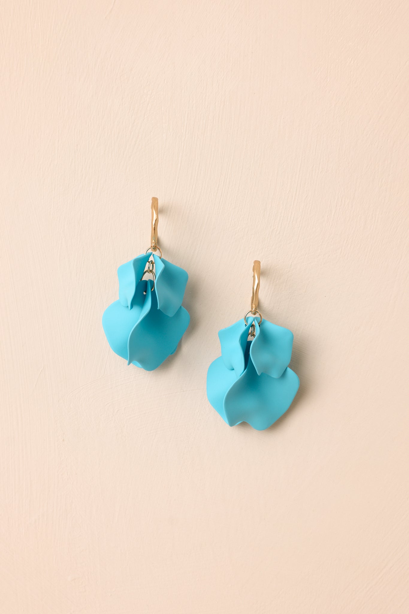 Layered petal drop earrings displayed against a beige background featuring matte gold-tone texture and curved shapes.
