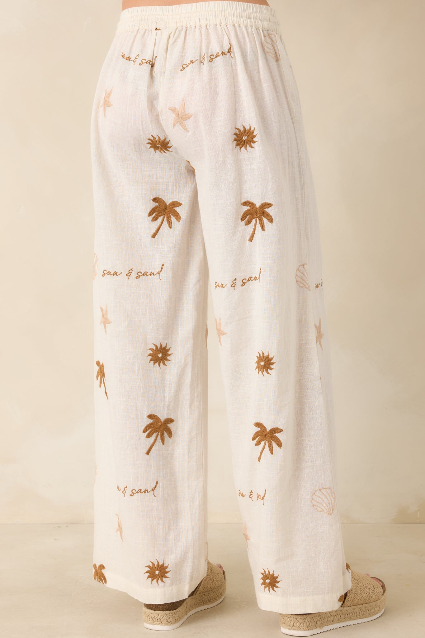 Light beige cotton pants with elastic waist and relaxed wide-leg rear silhouette.
