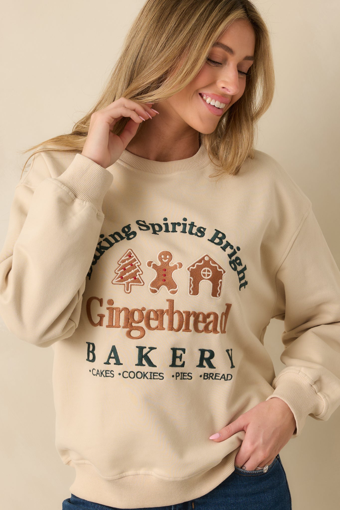Light beige fleece sweatshirt focusing on the dimensional gingerbread bakery embroidery.