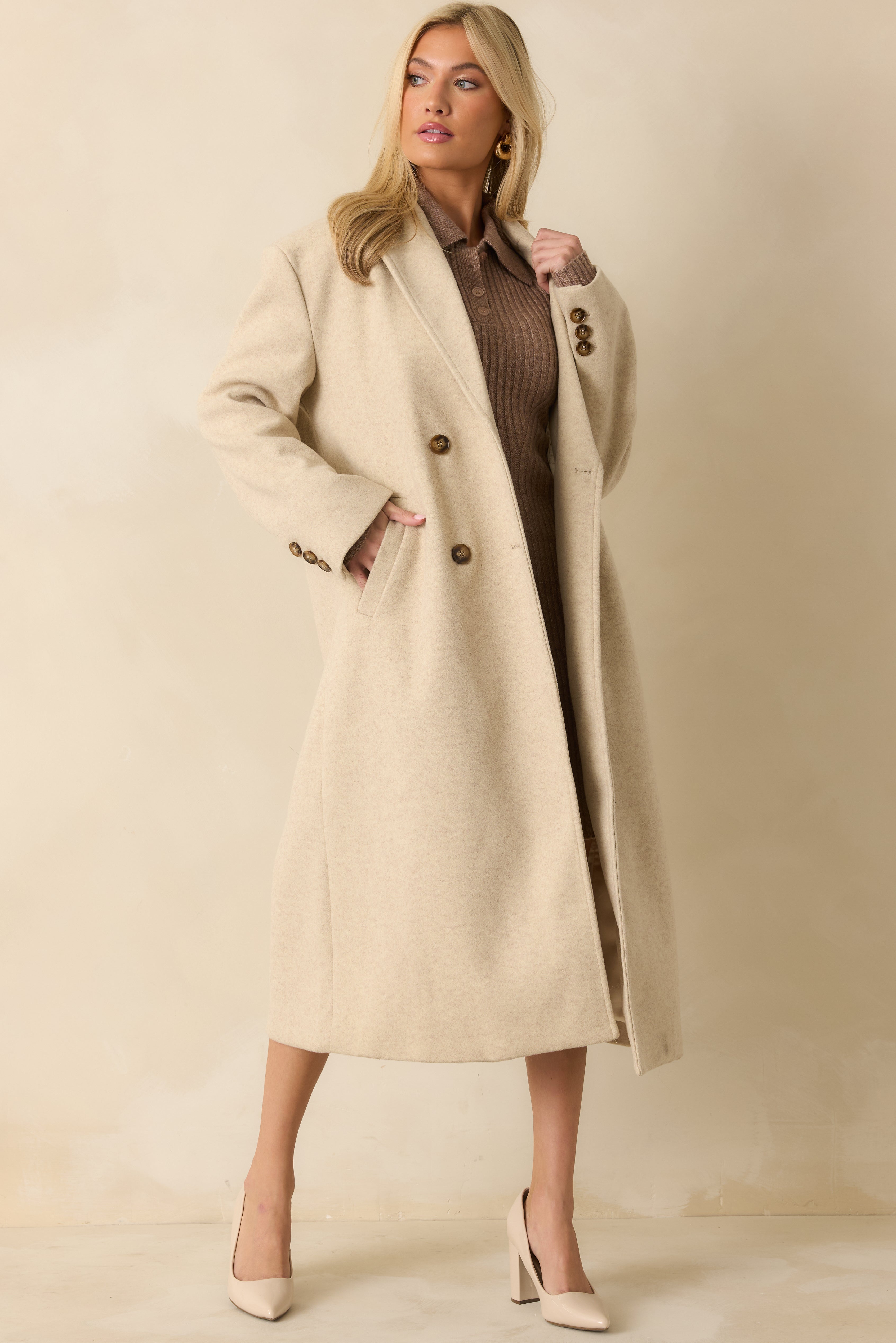 Light beige longline coat with a notched lapel, double-breasted tortoise buttons, and long sleeves with buttoned cuffs