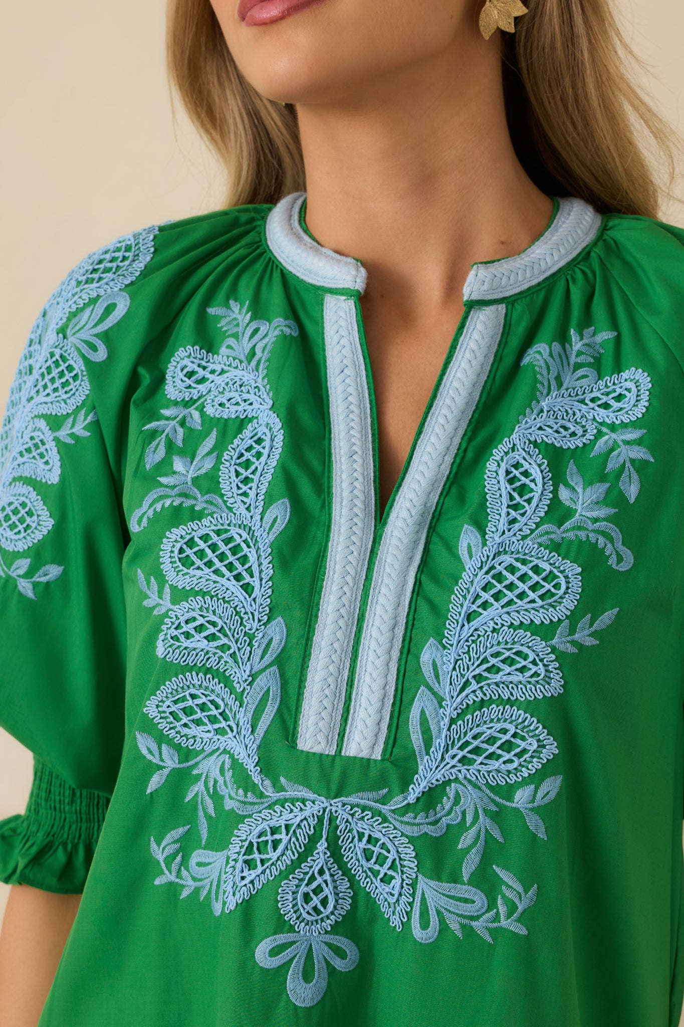 Close-up of light blue embroidery on the green maxi dress bodice and sleeve detailing.