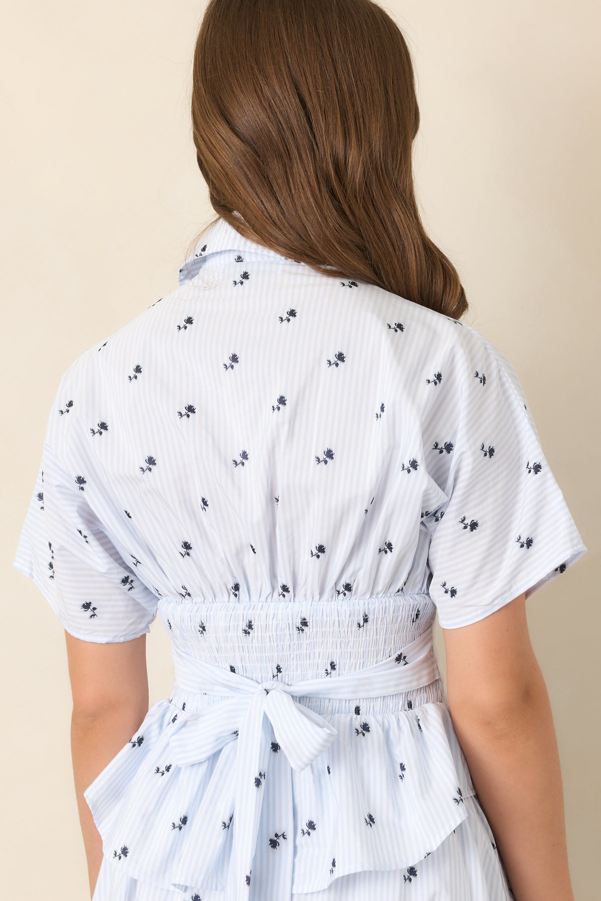Rear view of the light blue striped top featuring navy floral motifs, relaxed dolman sleeves, and a flared peplum hem.
