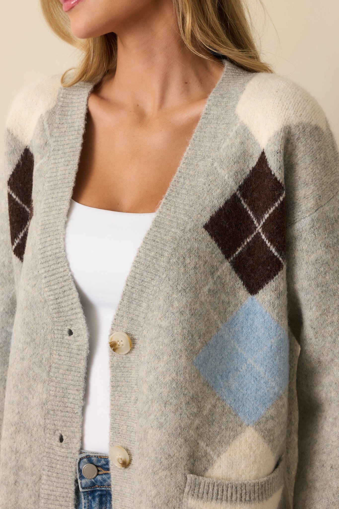 A close-up detail of the light grey cardigan showing the knit texture, ivory and brown argyle stitching, and button closure.