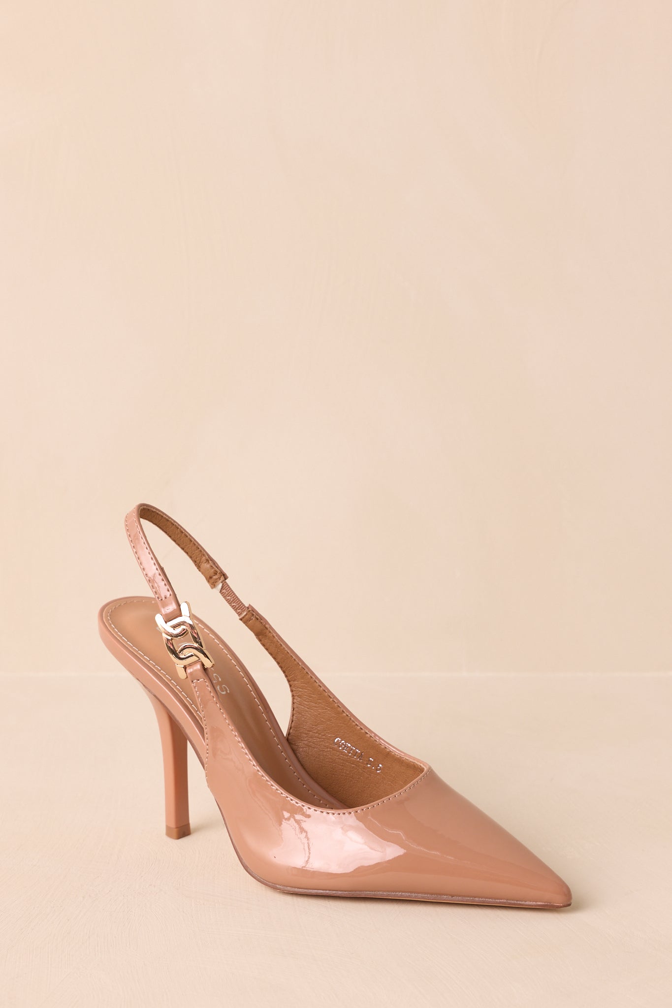 An angled front cropped view emphasizing the pointed toe and light mocha color of the patent upper.