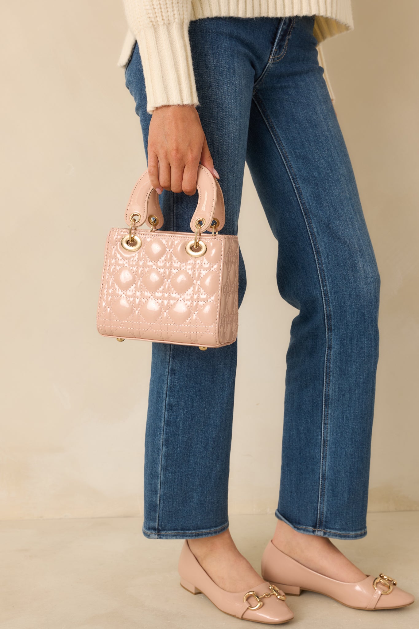 Full view of the light pink quilted faux patent leather handbag featuring a structured silhouette and top handles.