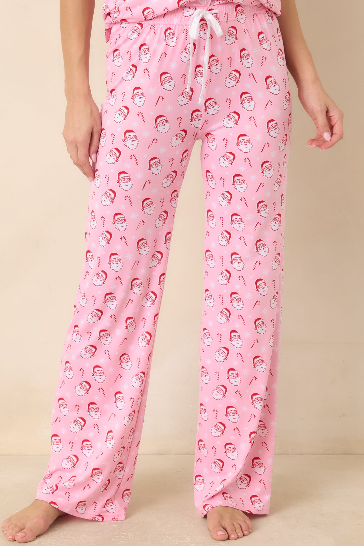 Light pink pajama pants display the allover Santa and candy cane print across the front.