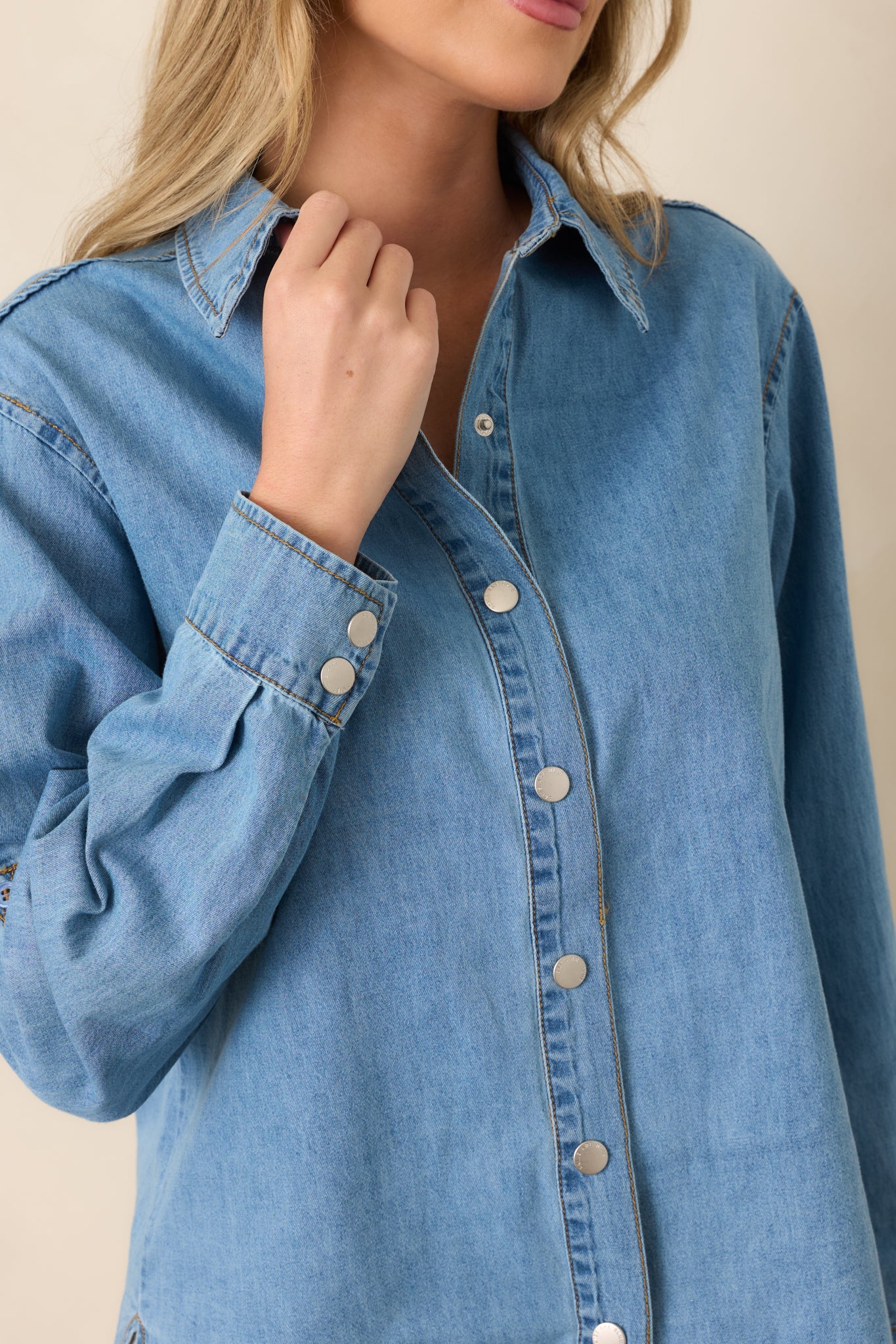 Close-up of the light wash cotton shirt highlighting the collared neckline, button-front closure, sleeve tab, and subtle fabric texture.
