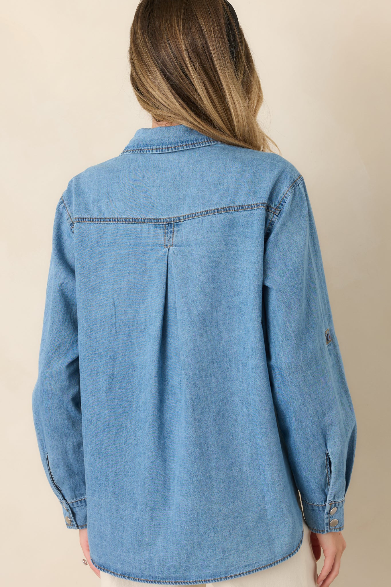 Rear view of the light wash cotton shirt showcasing the classic yoke-style back, relaxed silhouette, roll-tab sleeves, and curved high-low hem.