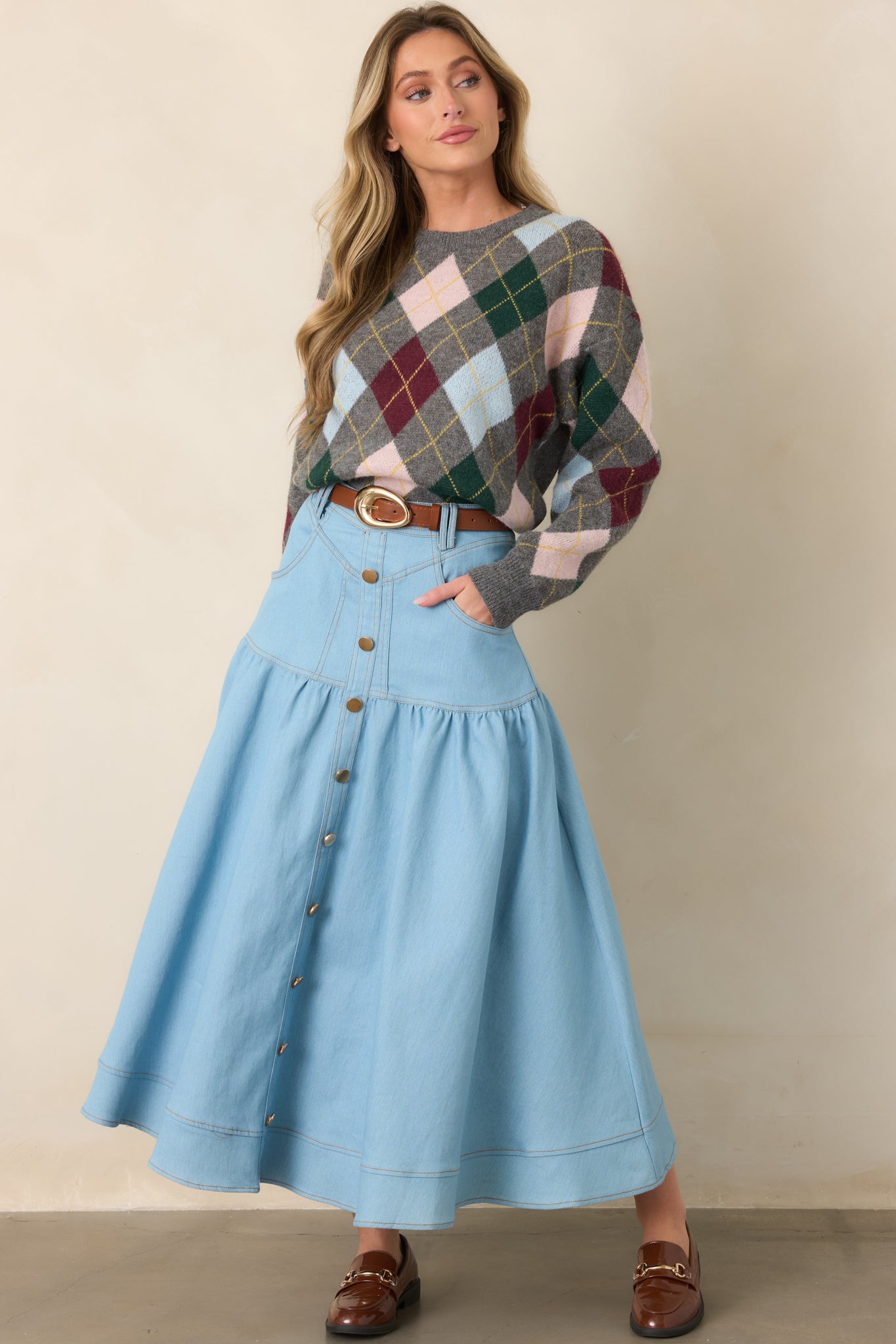 Light wash denim maxi skirt with a high-rise waistband, gold-tone button-down front, tiered construction, and softly flared silhouette.