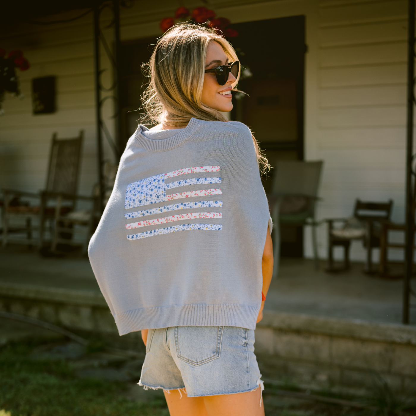 Woman wearing a light blue sweater with an American flag design outdoors.