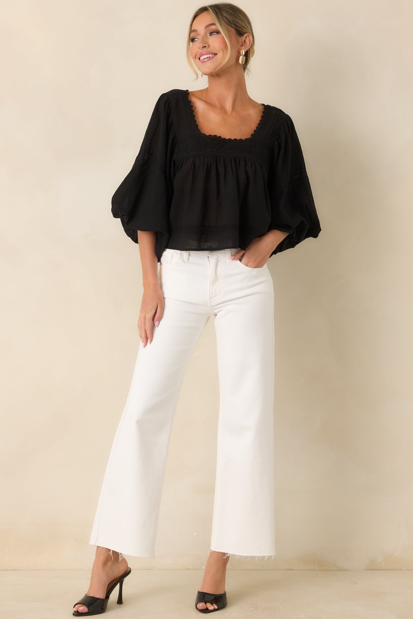 Full-length view of a lightweight cotton blouse featuring a gathered square neckline, scalloped trim, lace inset detailing, voluminous puff sleeves, and a relaxed drape through the body.
