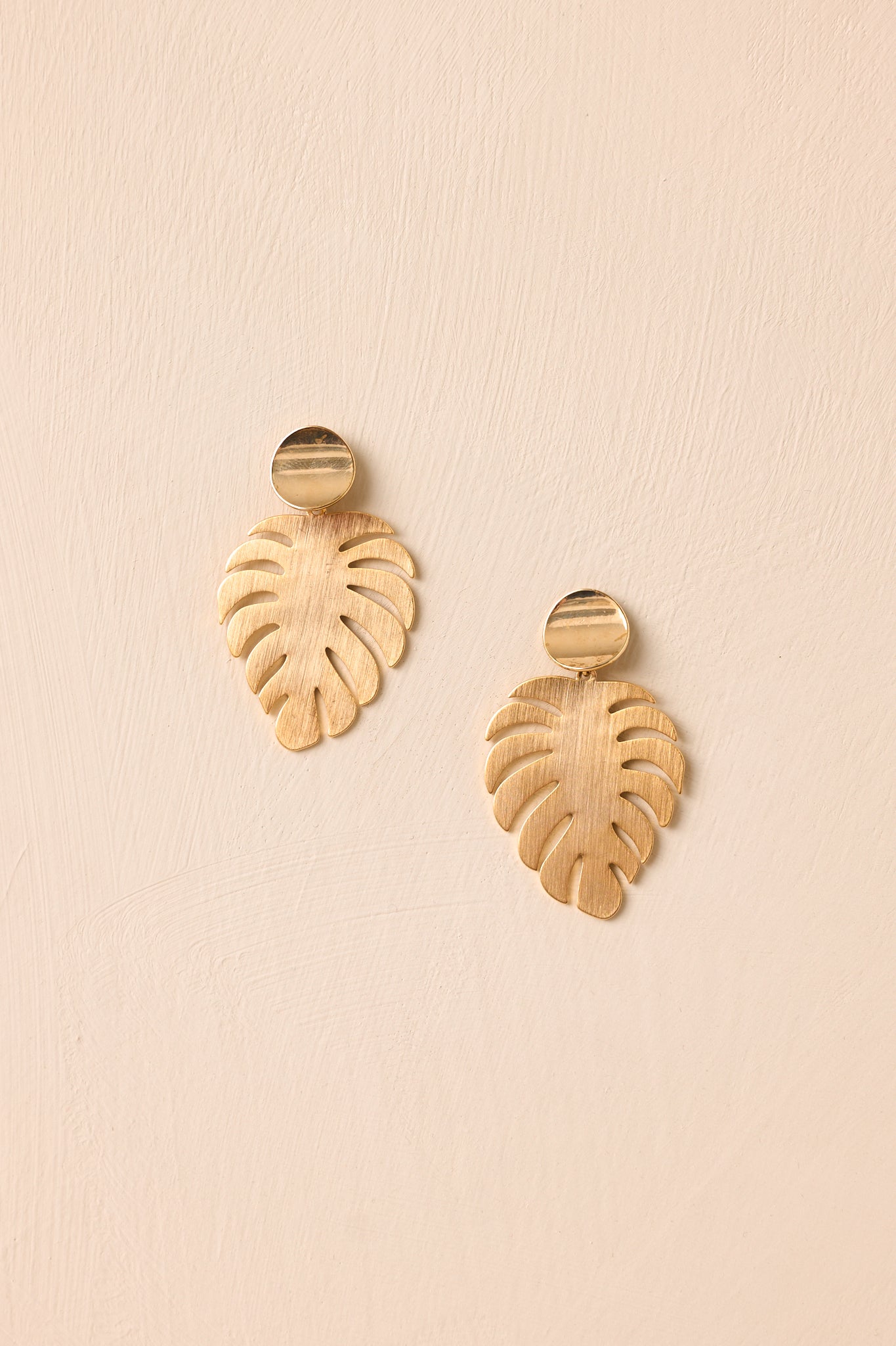 Lightweight gold earrings with a round disc top and brushed leaf-inspired hanging detail.