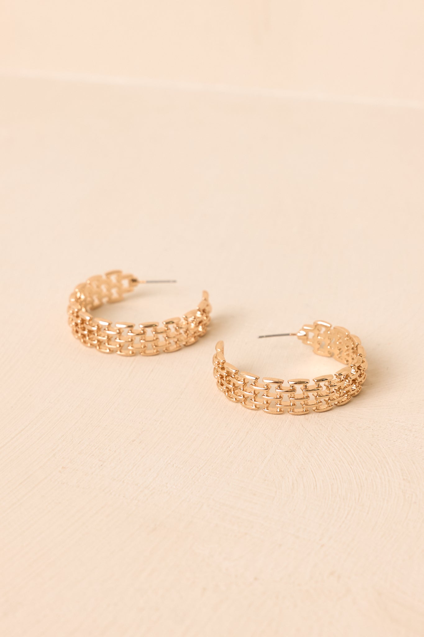 Pair of lightweight gold-tone hoop earrings featuring intricate chain mesh detailing against a neutral beige background.