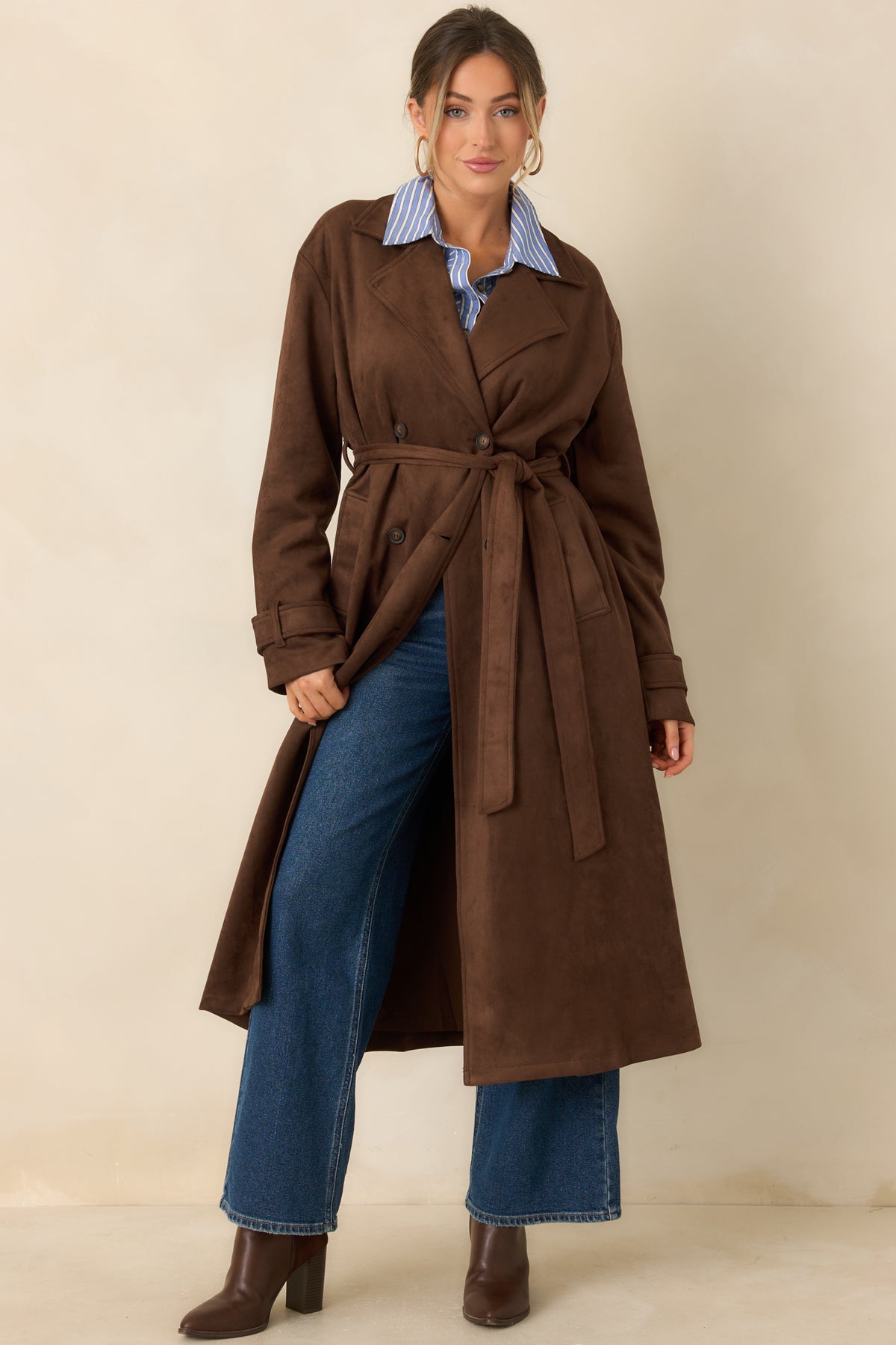 Classic longline coat displays a notched collar, symmetrical double-breasted buttons, and a softly shaped waist with a matching belt.