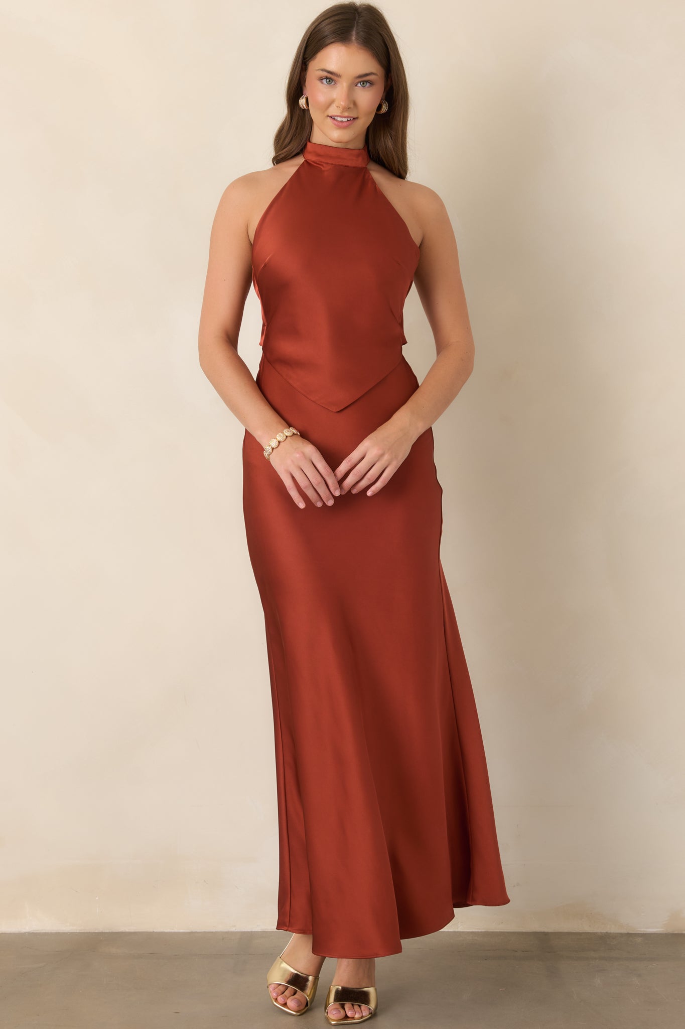 Lustrous burnt sienna maxi dress with a sculpted halter neckline, pointed overlay across the bodice, and gracefully draped skirt.