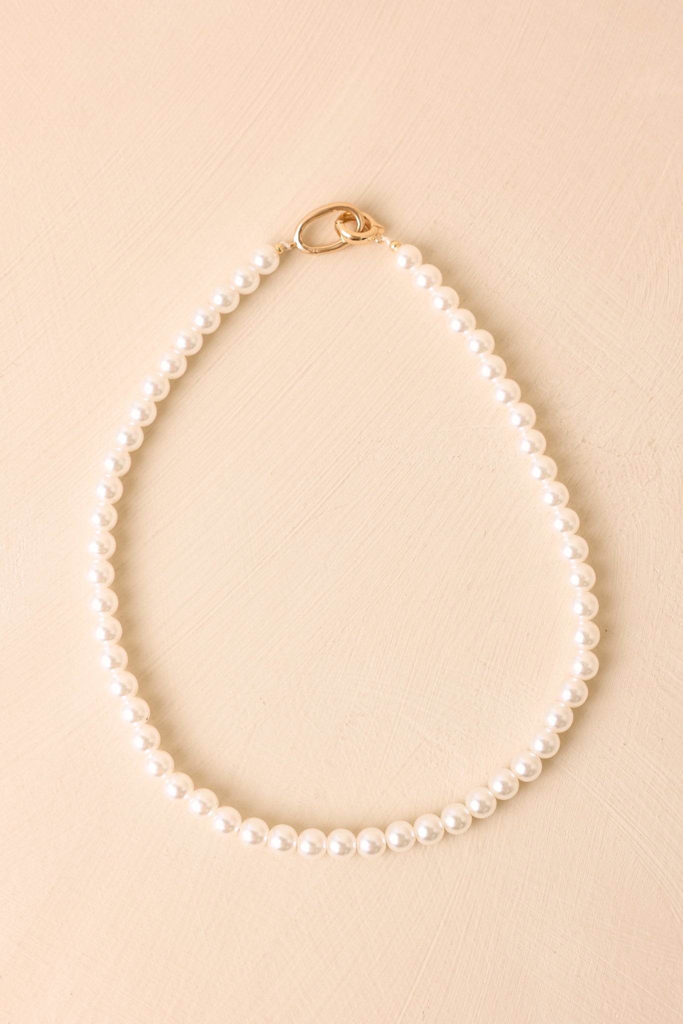 Strand of lustrous faux pearls arranged against a beige background with the polished gold-tone hinged clasp on display.