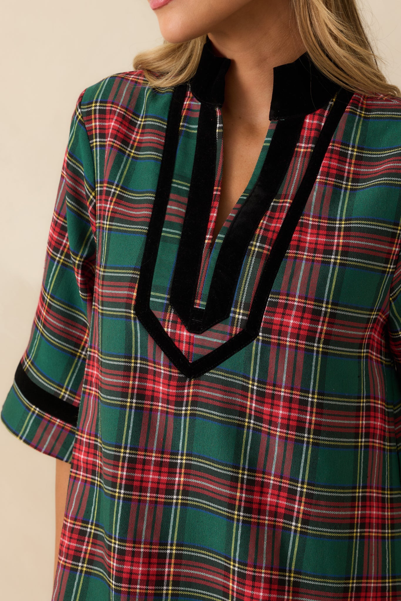Macro view of green plaid fabric, black velvet trim, and split neckline detailing on the mini dress.