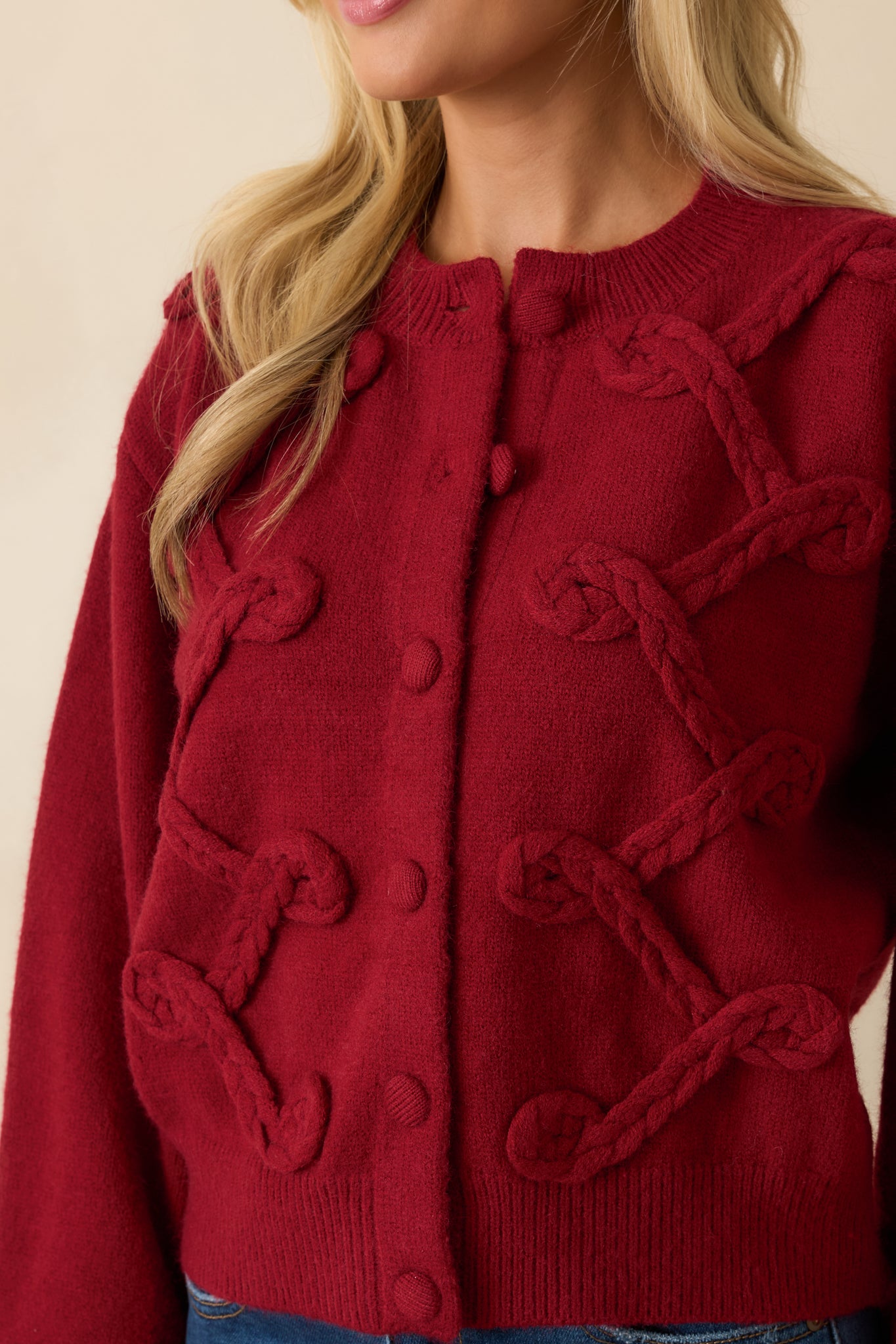 Macro view of the thick braided appliqué, ribbed trim, and button closure on the red knit cardigan.