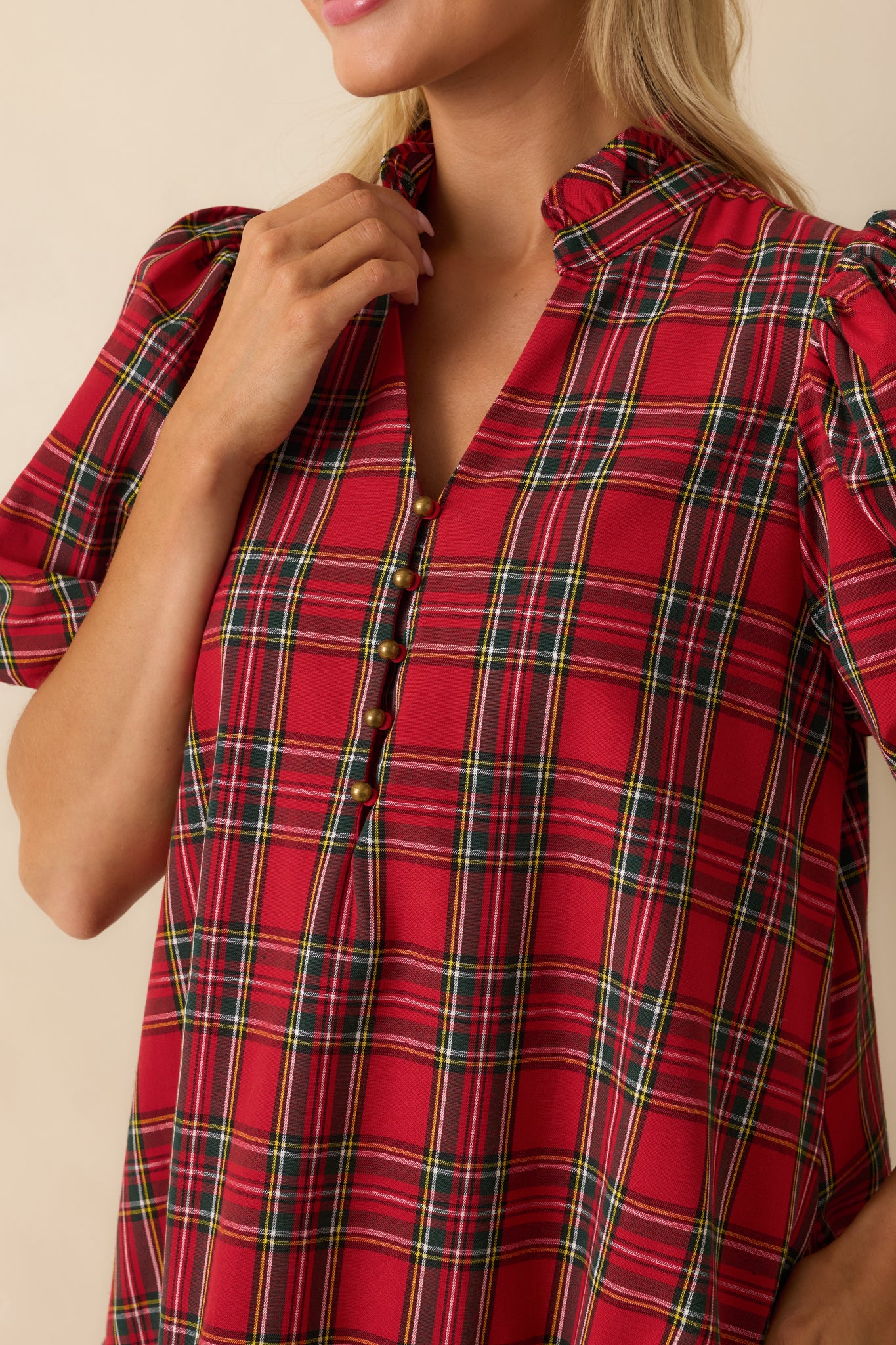 Macro view of red plaid fabric, split neckline with button detail, ruffled hem, and puff sleeve texture on the mini dress.