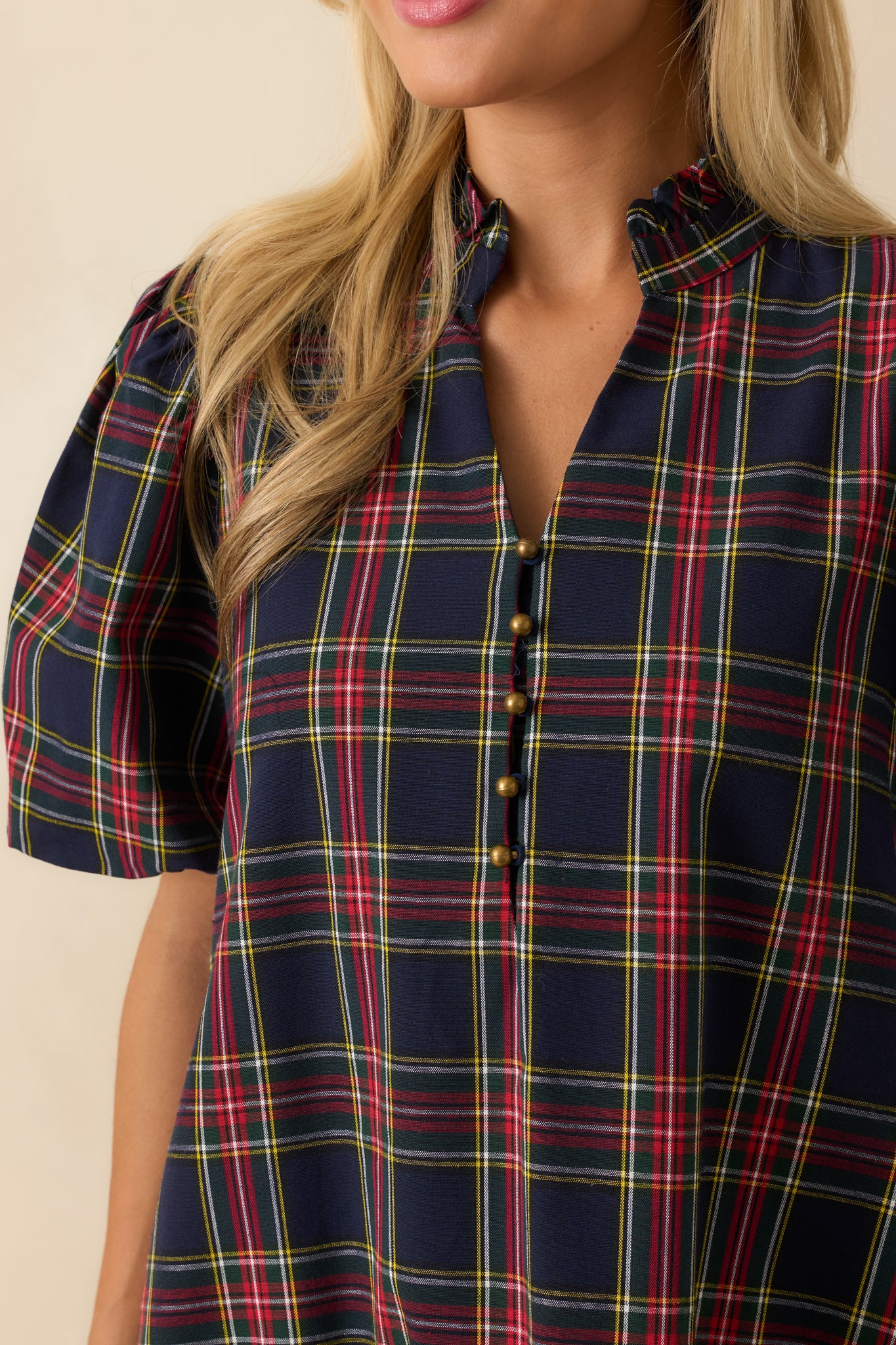 Macro view of navy plaid fabric, split neckline with button detail, ruffled hem, and puff sleeve texture on the mini dress.