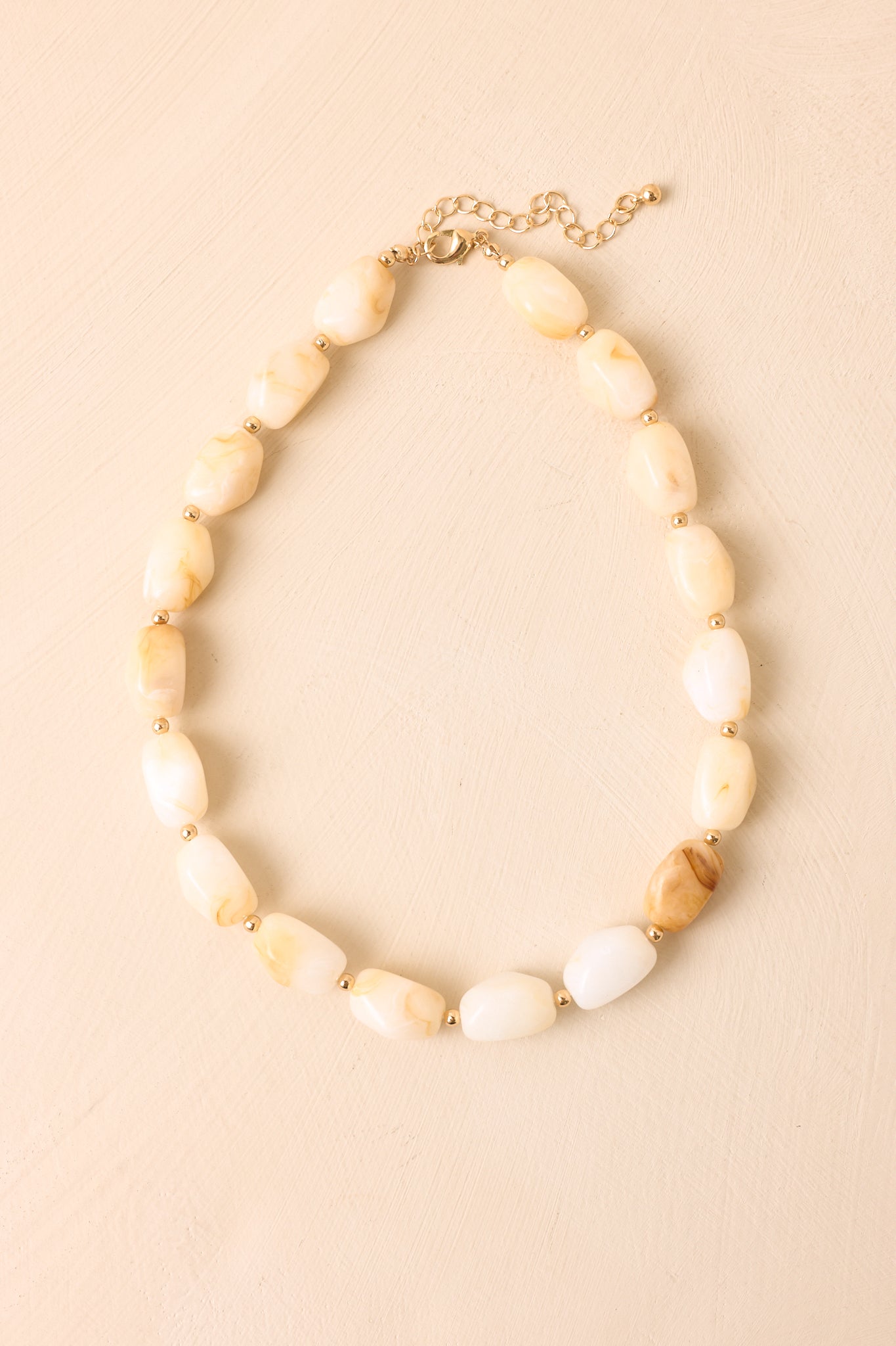 Marbled bead necklace displayed against a beige background, highlighting the organic shapes and polished spacer details.