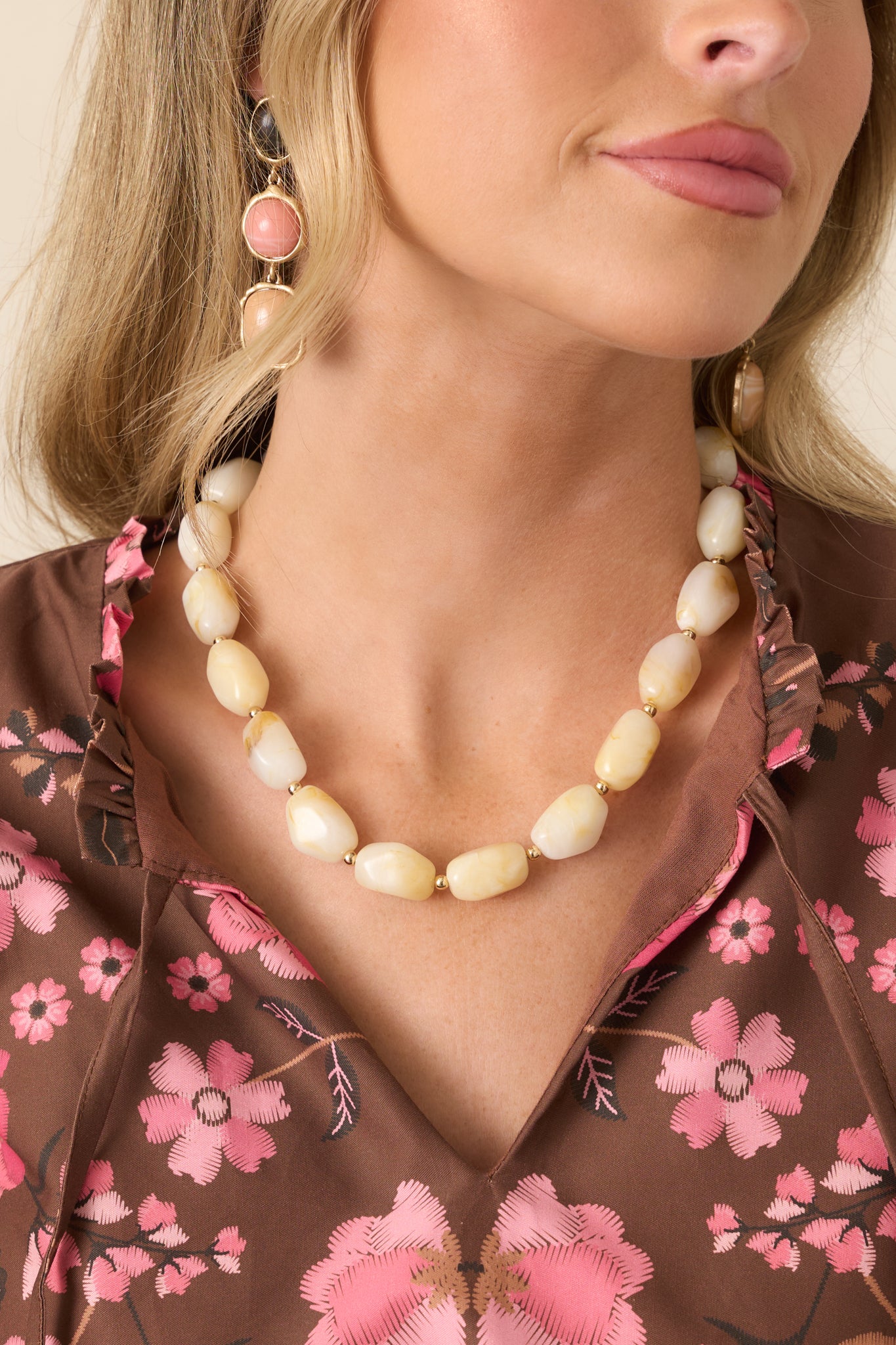 Statement necklace featuring marbled cream resin beads in organic shapes, separated by polished gold-tone spacer beads.