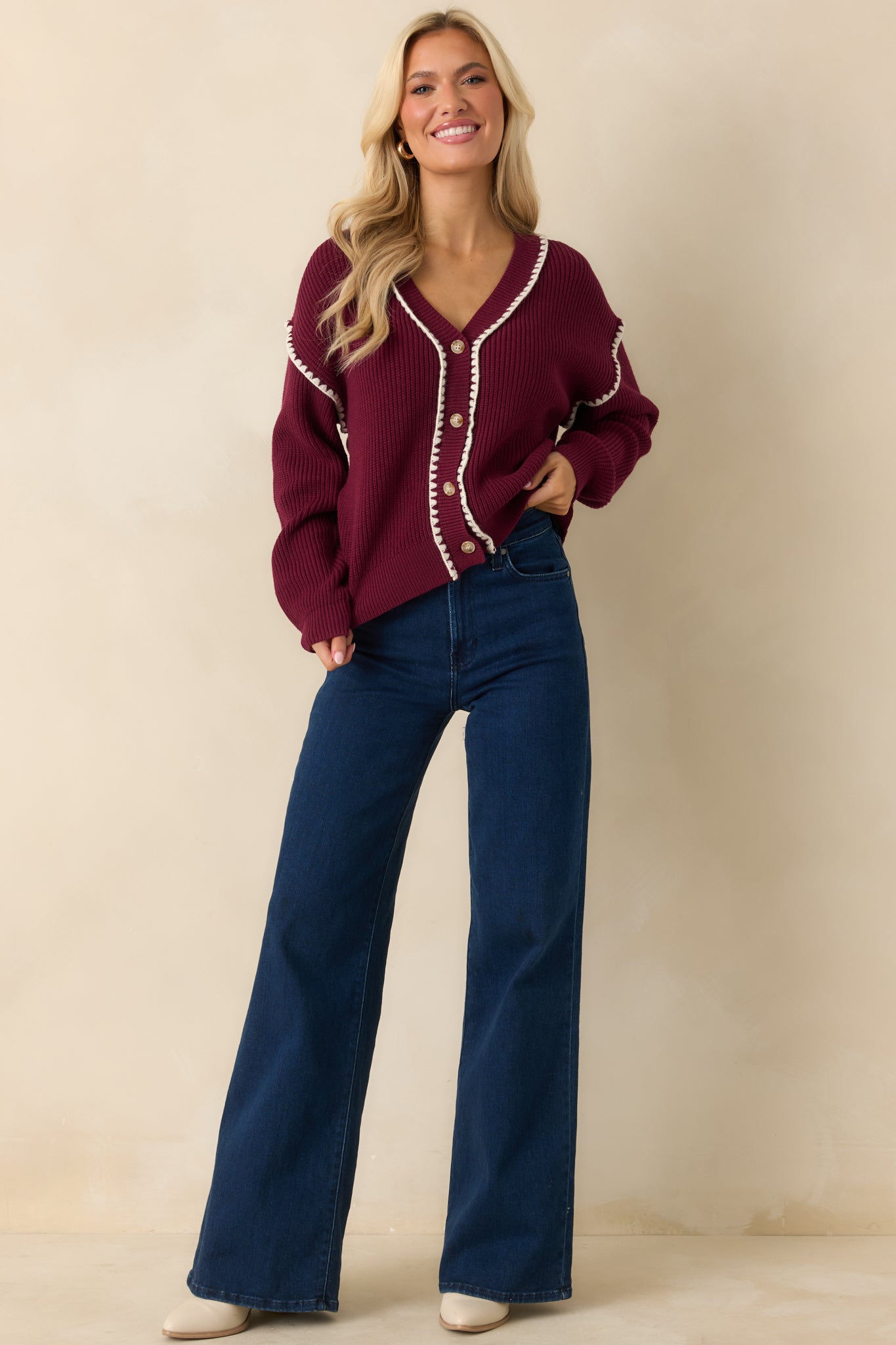 The maroon cardigan shows its functional button front, ribbed knit texture, and v-neckline with white whipstitch trim.