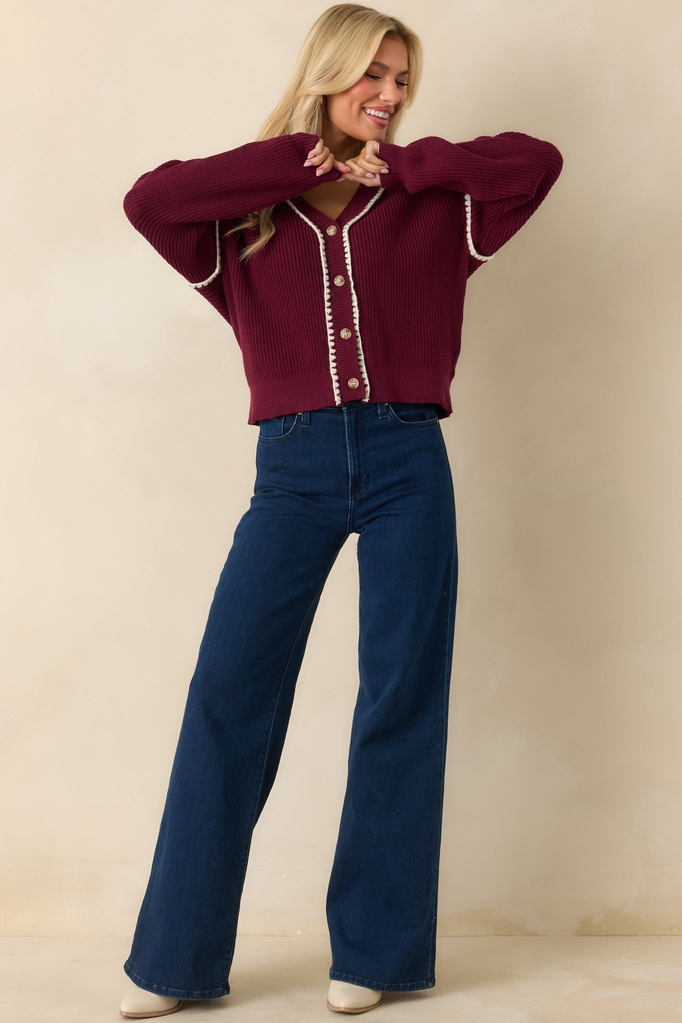 The cardigan displays its maroon ribbed knit fabric with a v-neckline, button-front closure, and white whipstitch trim along all edges.