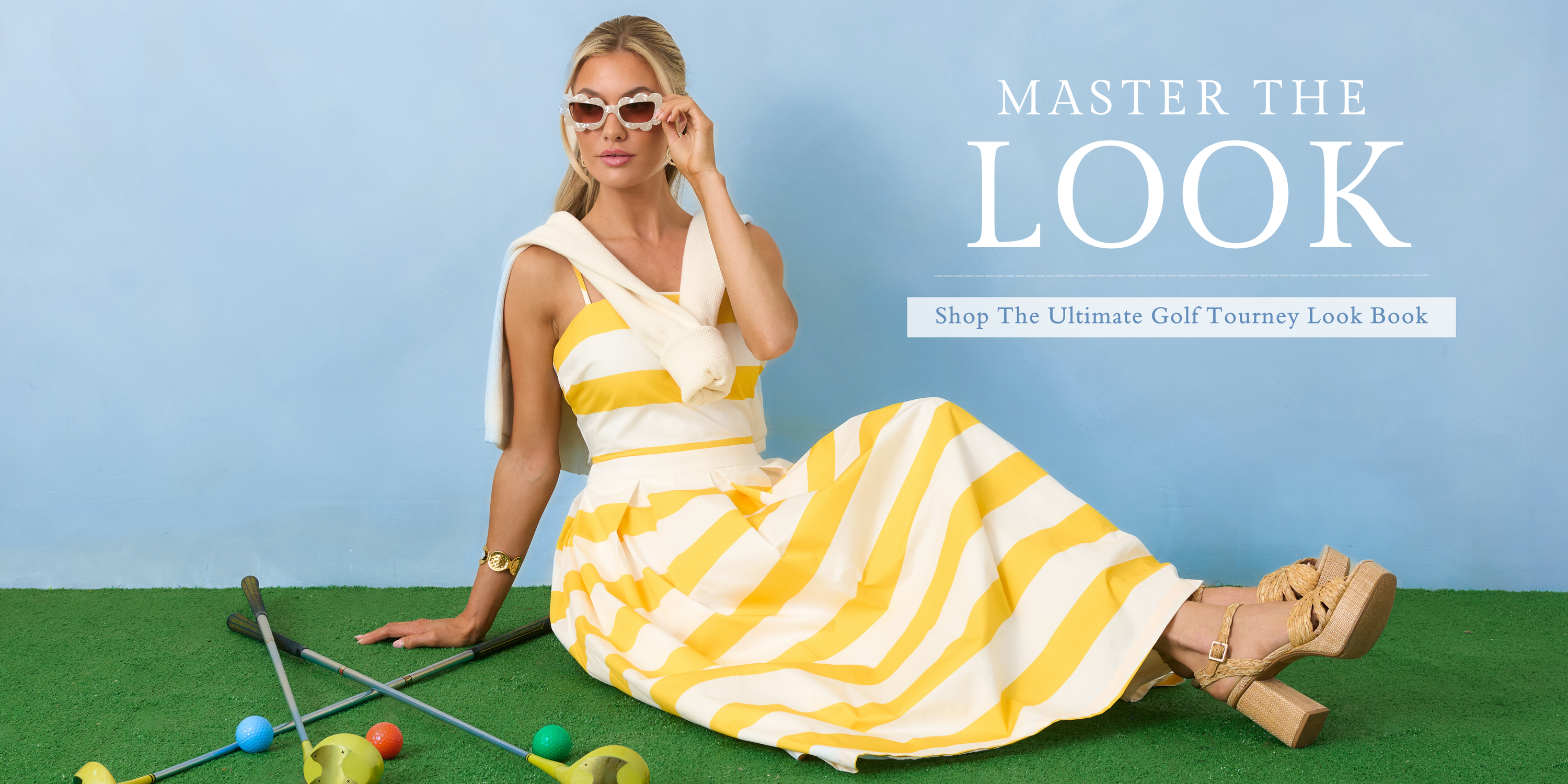 Model sitting on green turf wearing a yellow and white striped midi dress styled with sunglasses and wedge heels in our Master The Look campaign. This image links to shop the Ultimate Golf Tourney Look Book featuring chic spring styles inspired by golf tournament fashion.