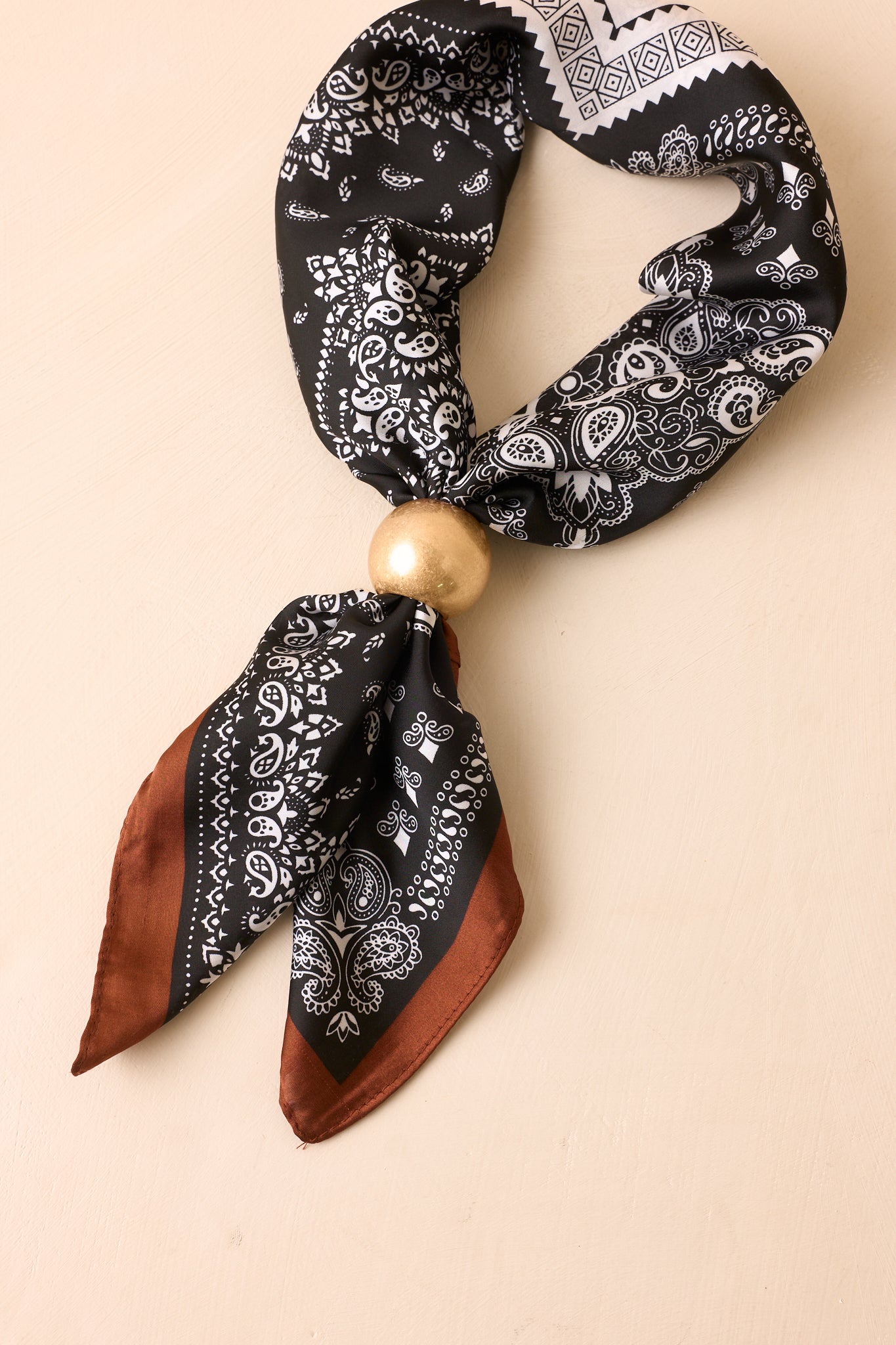 Matte gold scarf ring displayed against a beige background, highlighting the smooth ball design and softly brushed metallic finish.