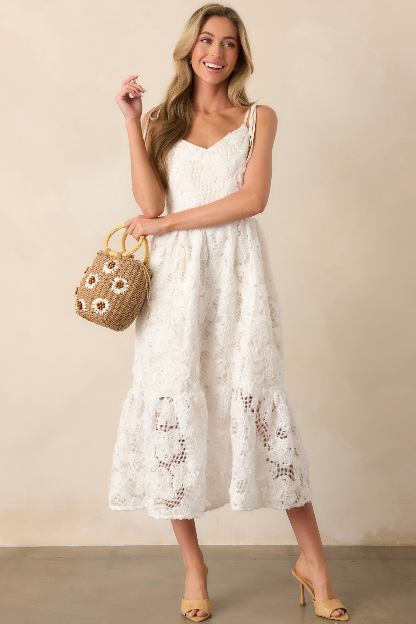 A maxi dress with a 3D floral lace overlay, ivory mini-length lining, and a deep V-neckline. The adjustable self-tie bow straps add a delicate touch to the design.
