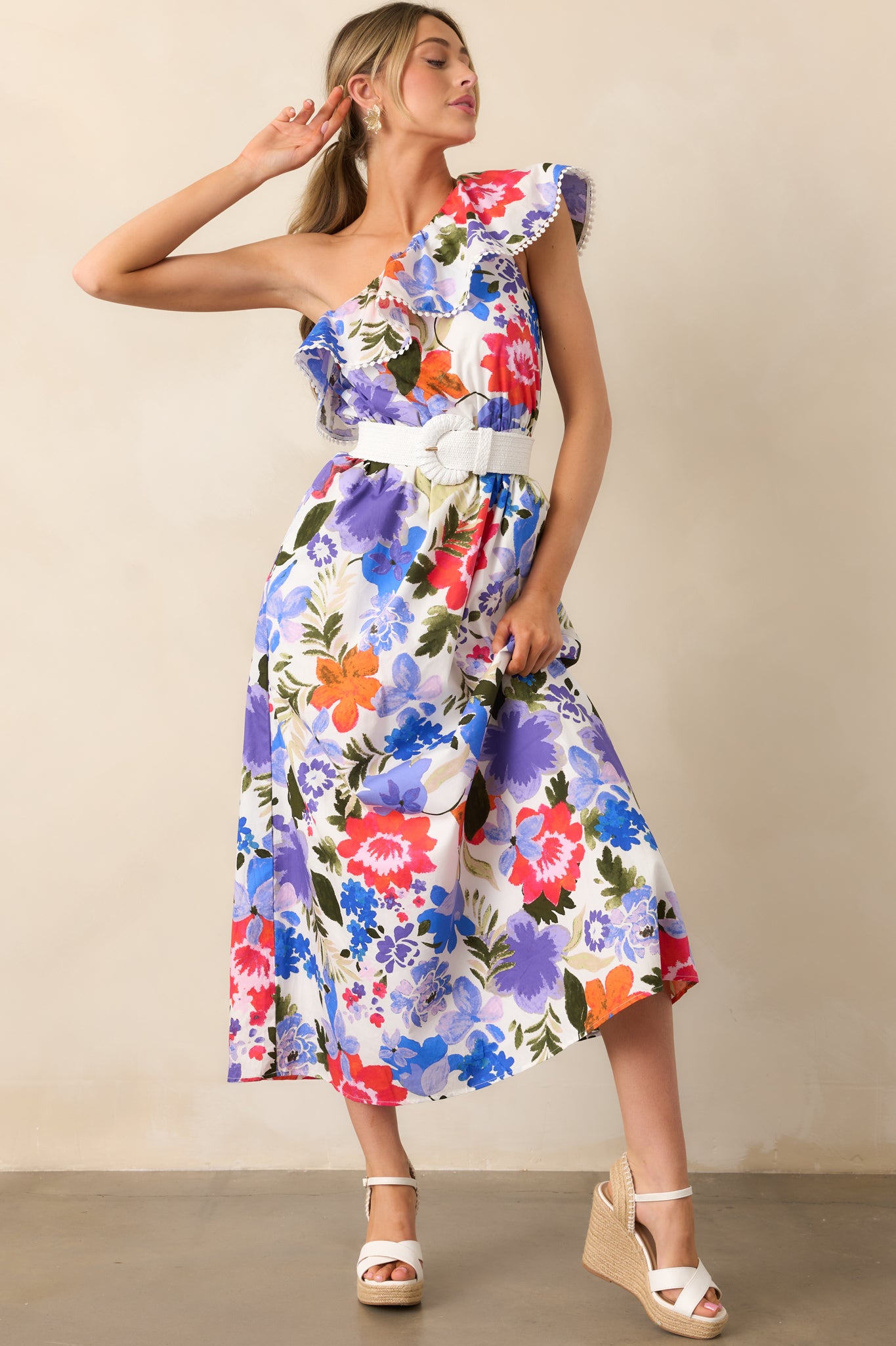 A front-facing shot of the maxi dress with an elastic one-shoulder ruffle neckline and vibrant blue and red floral print, complemented by an elastic waist and functional pockets.