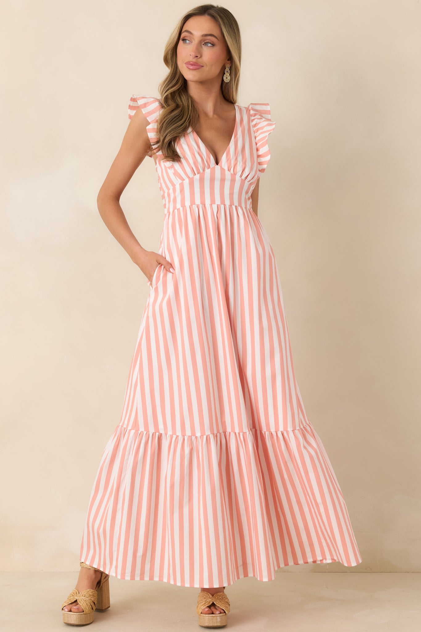 Romantic maxi dress with deep V-neck, fluttering wide straps, and a flowing tiered skirt that emphasizes length and movement.