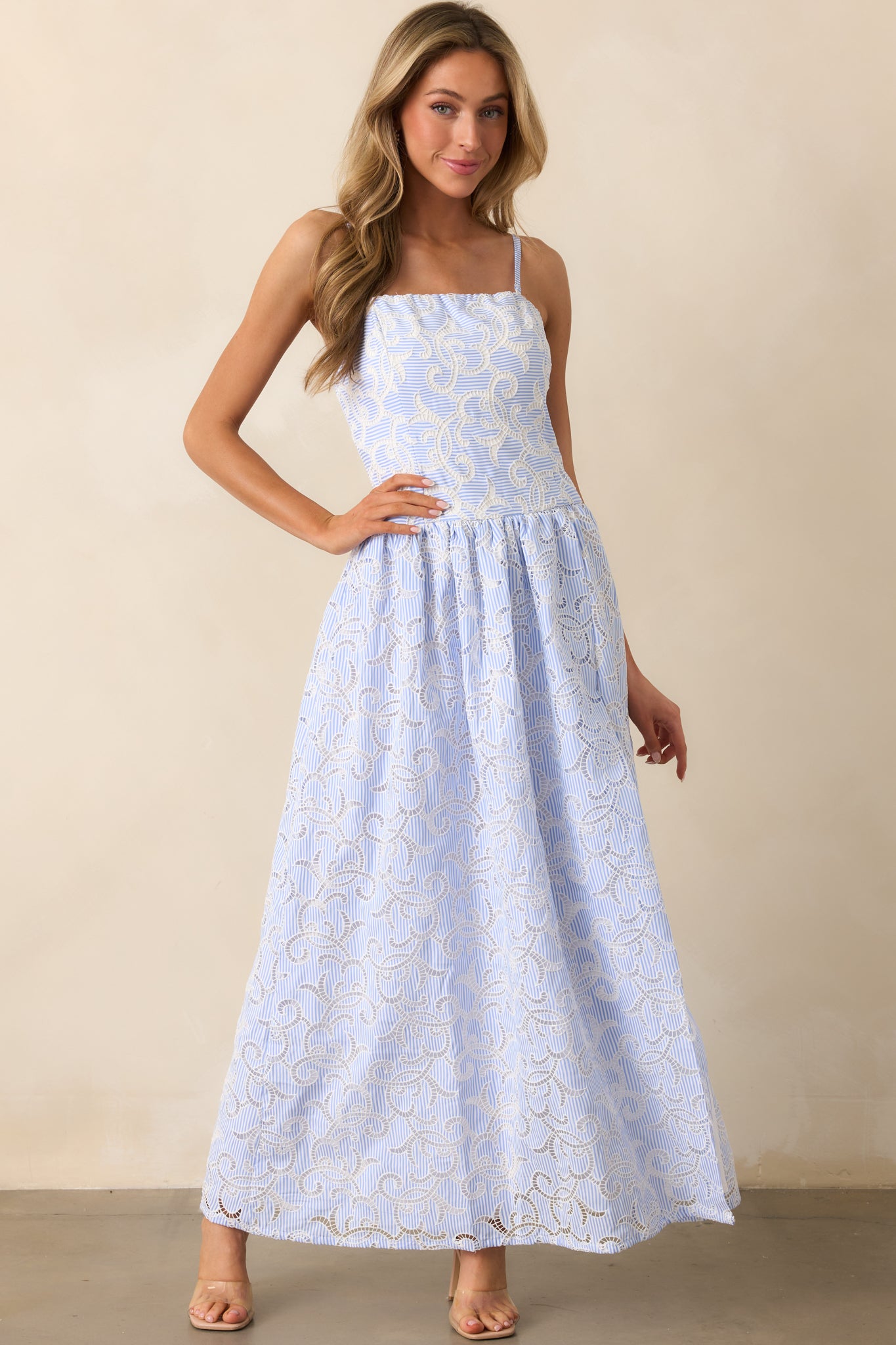 A breezy maxi dress with a blue and white striped design, embroidered details, and a smocked back panel. The dress moves gracefully, showcasing its lightweight fabric and full-length silhouette.