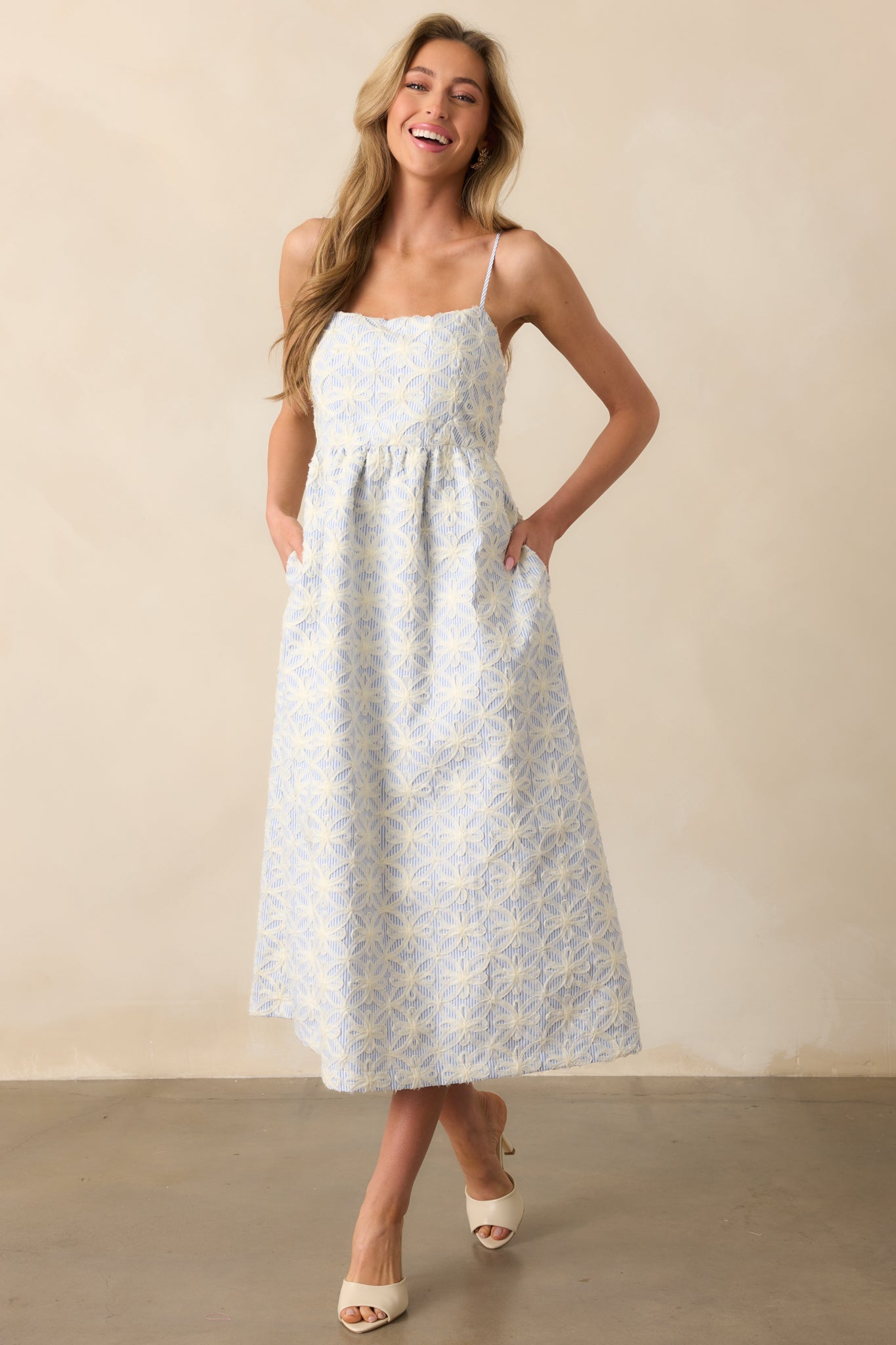  A front-facing view of the blue and white striped maxi dress with 3D floral appliqués, square neckline, and functional pockets, designed with adjustable spaghetti straps.