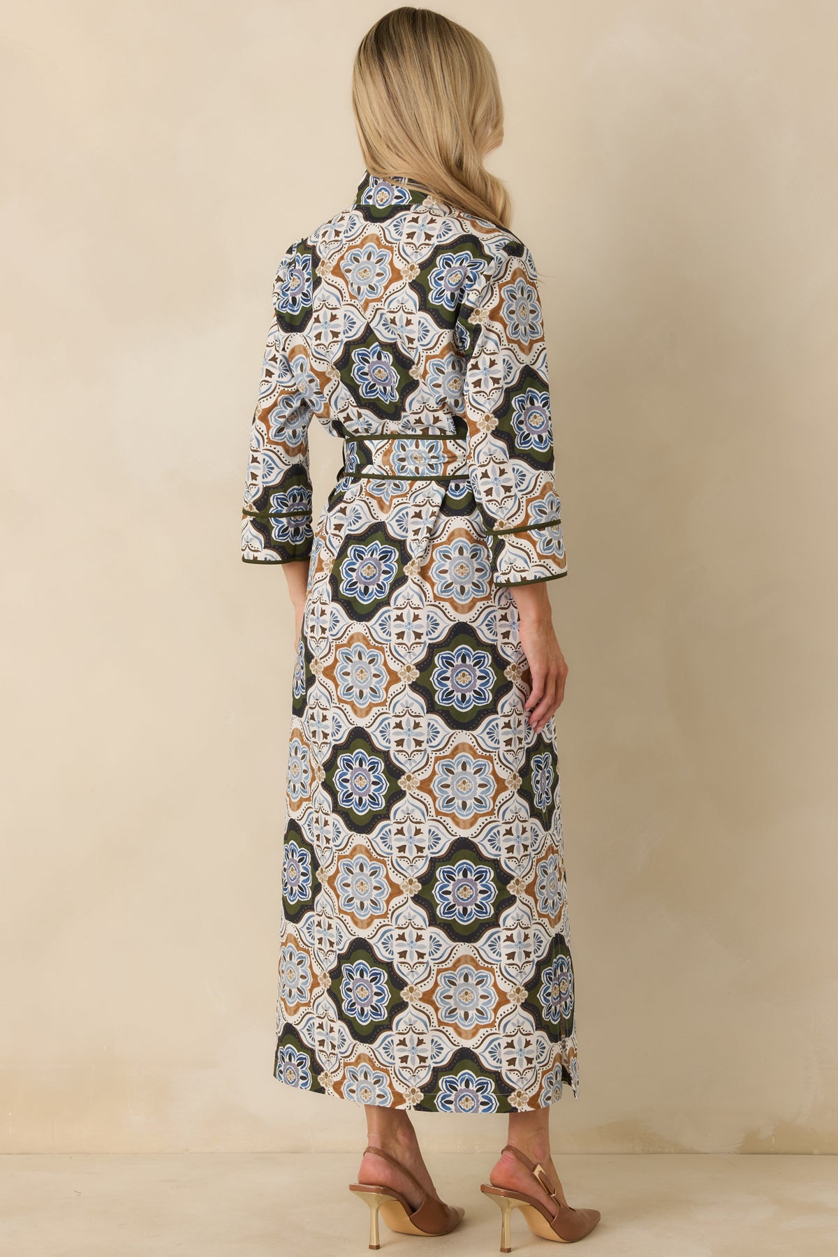 Back view of a medallion print maxi dress with a structured collar, three-quarter sleeves, olive piping, and belted waist.