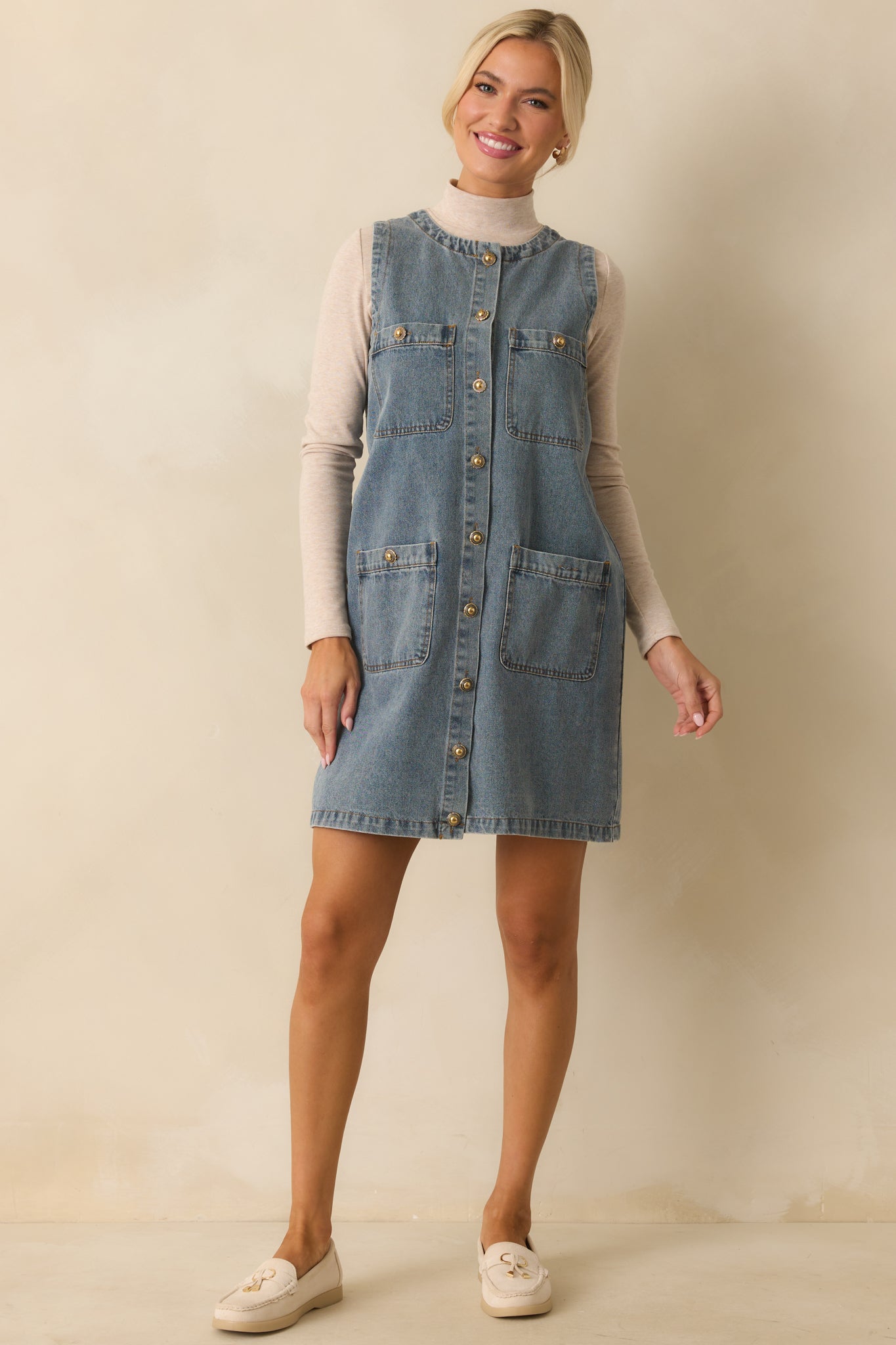 A front view of the medium-wash denim mini dress with a sleeveless design, round neckline, and button-front closure.