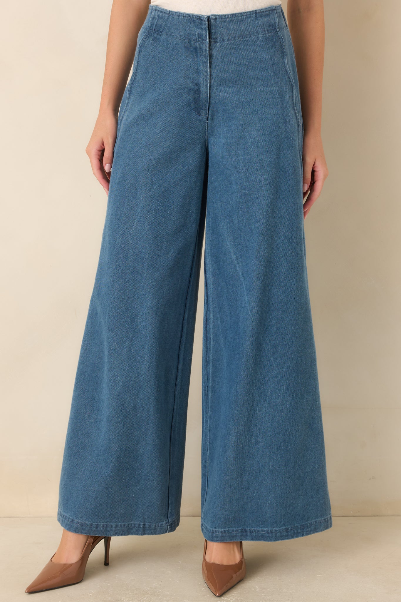 Medium wash denim jeans highlighting the high-rise waistband, hidden zip closure, and curved scalloped side seam detailing.