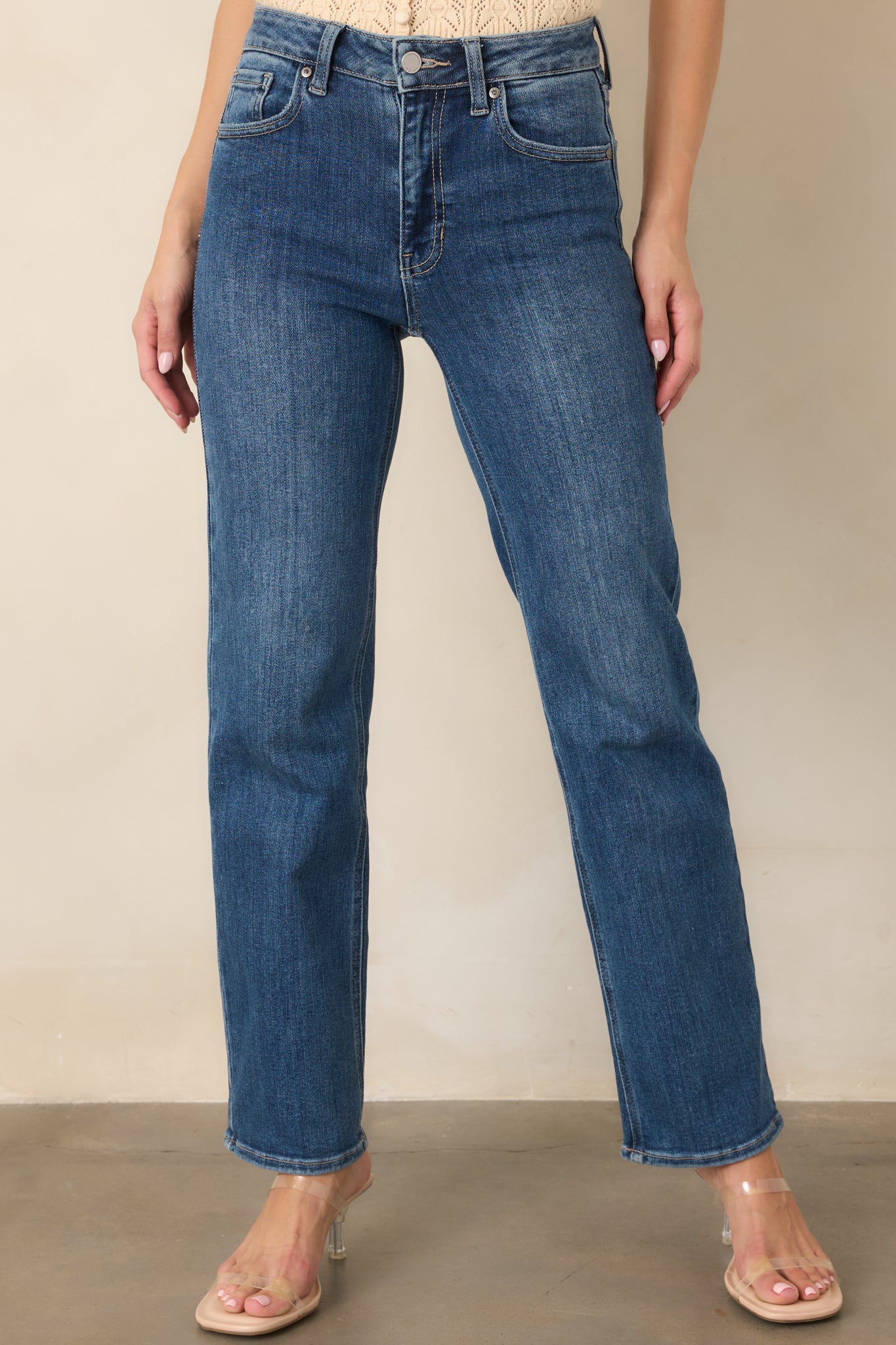 Close view of the medium wash jeans highlighting the high-rise waistband, belt loops, front pockets, and button-and-zip fly.