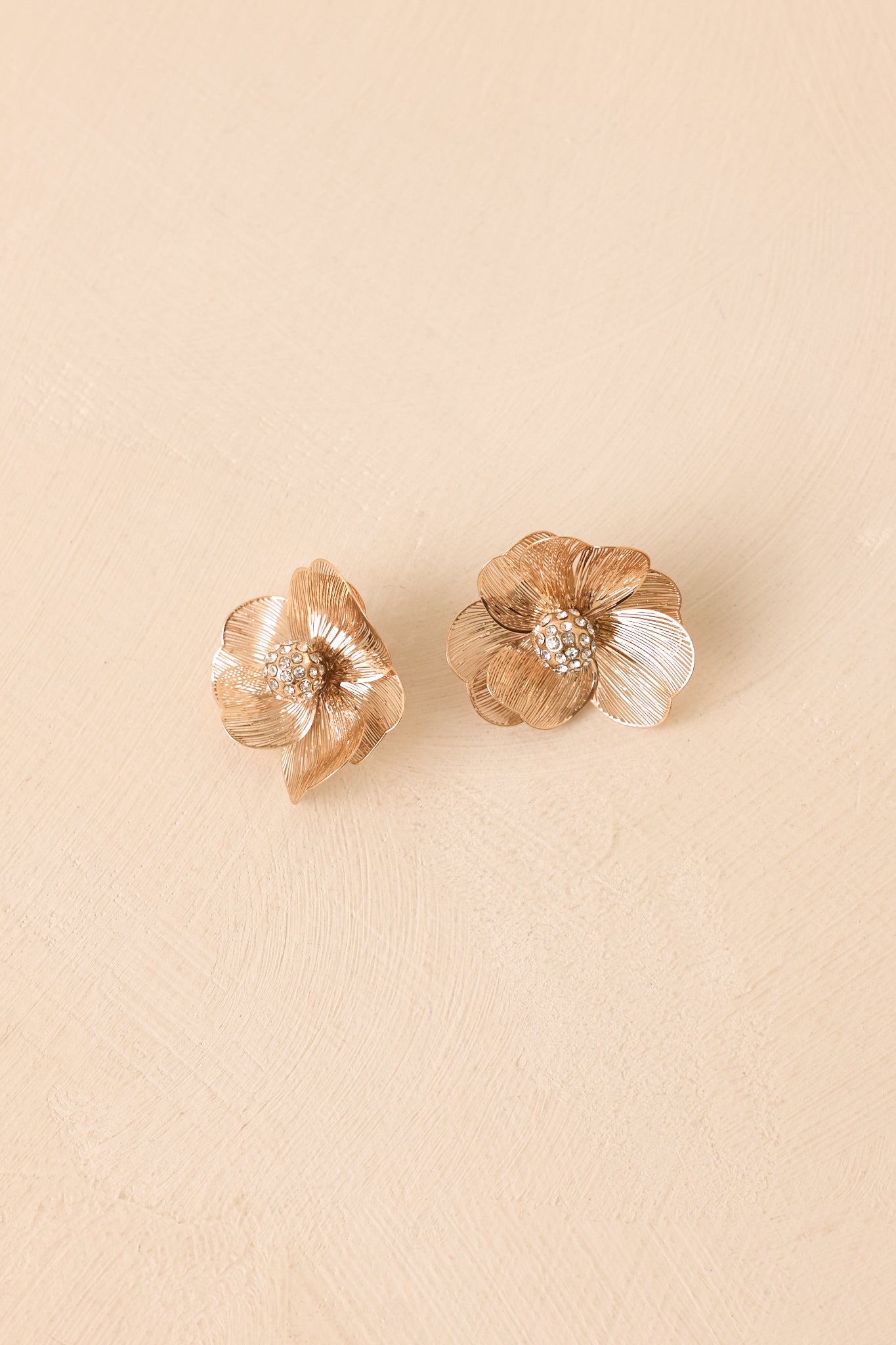 Metallic floral stud earrings on a beige background highlighting the gold finish and sparkling centers.