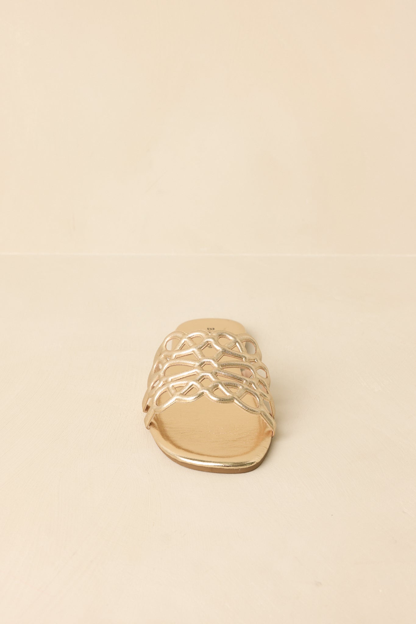 Metallic gold slide sandals with an open-toe design and wide cutout strap, set on a flat sole