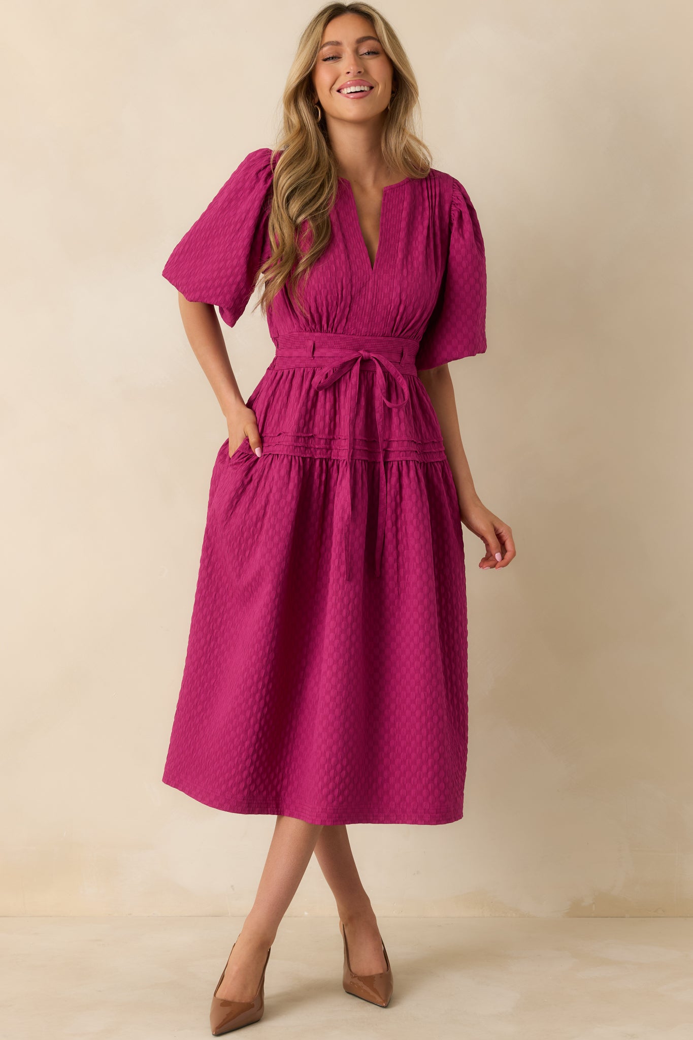 The midi dress shows its split neckline, short puff sleeves, and pleated bodice with an adjustable tie waist.