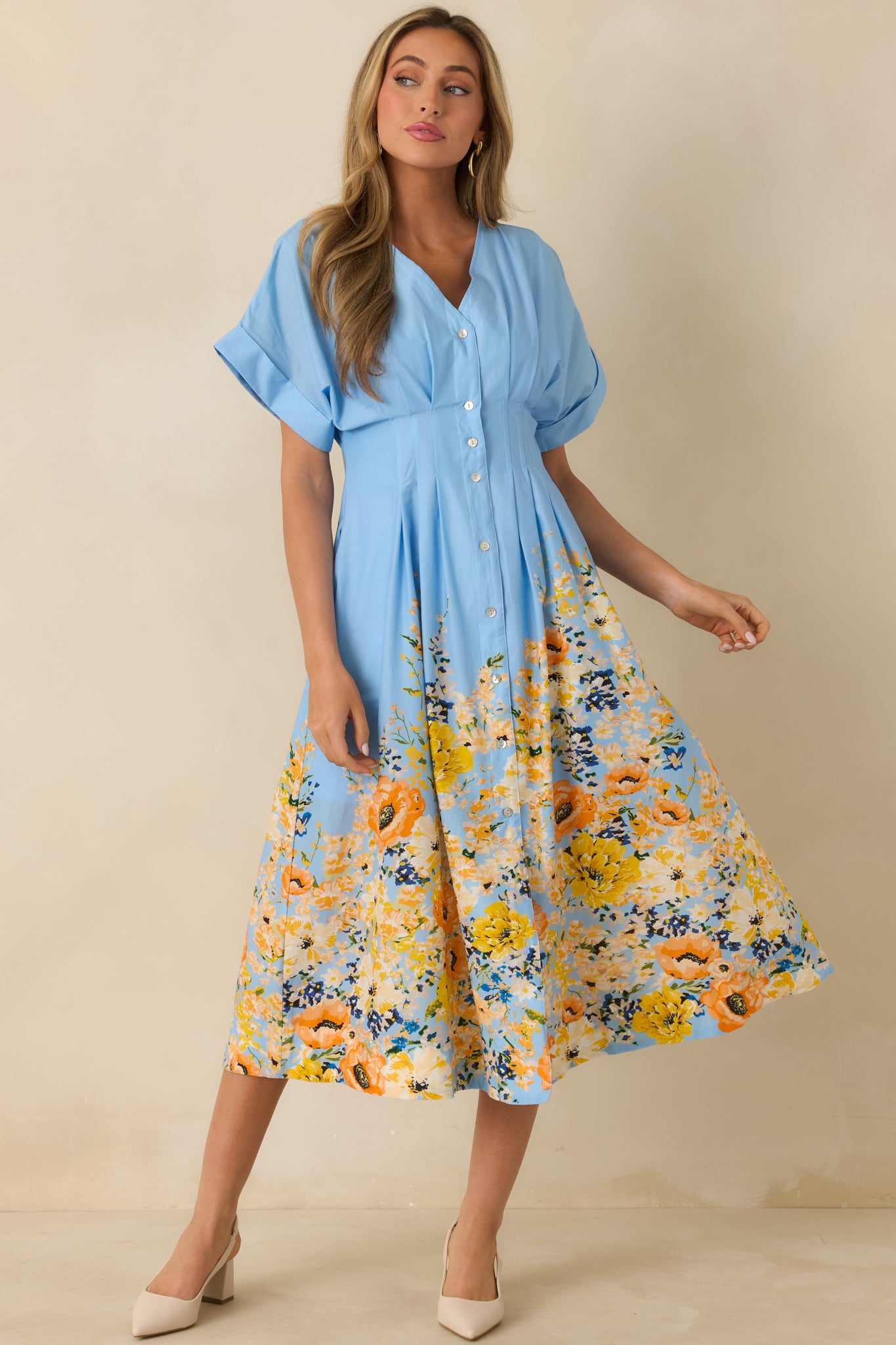 Flowing blue cotton midi dress with floral hem detail, short flutter sleeves, and button-down front, emphasizing waist shape.