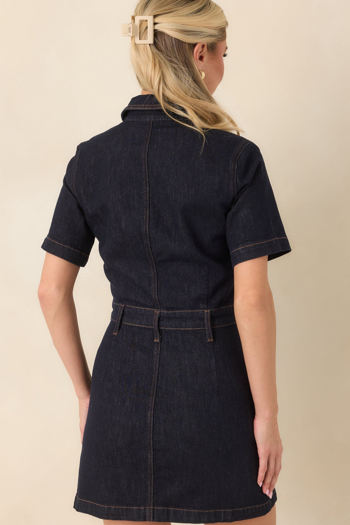 Rear of the midnight wash denim mini dress displays the short sleeves, collared neckline, and fitted waist.