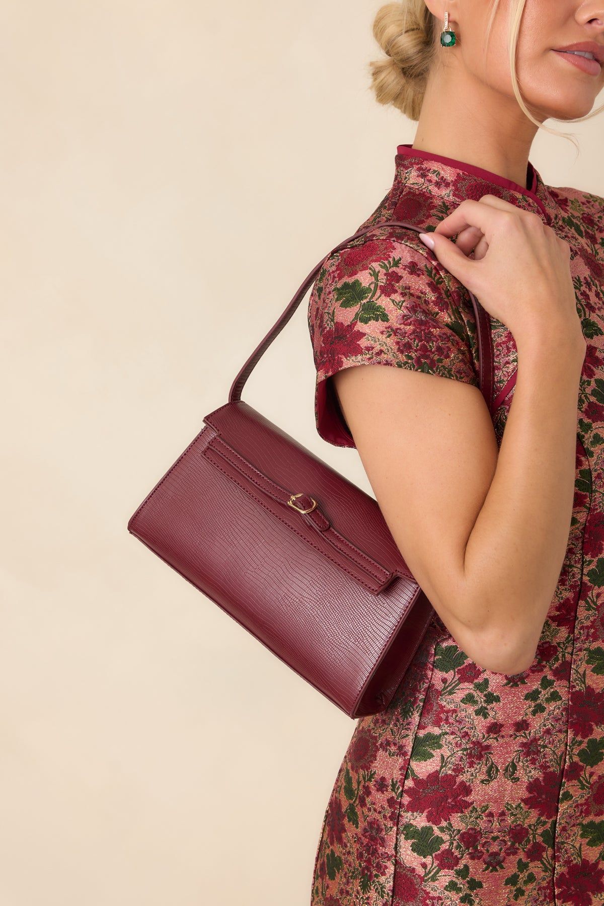Minimalist handbag displays a slim strap, geometric shape, and polished gold-tone hardware against a finely textured exterior.